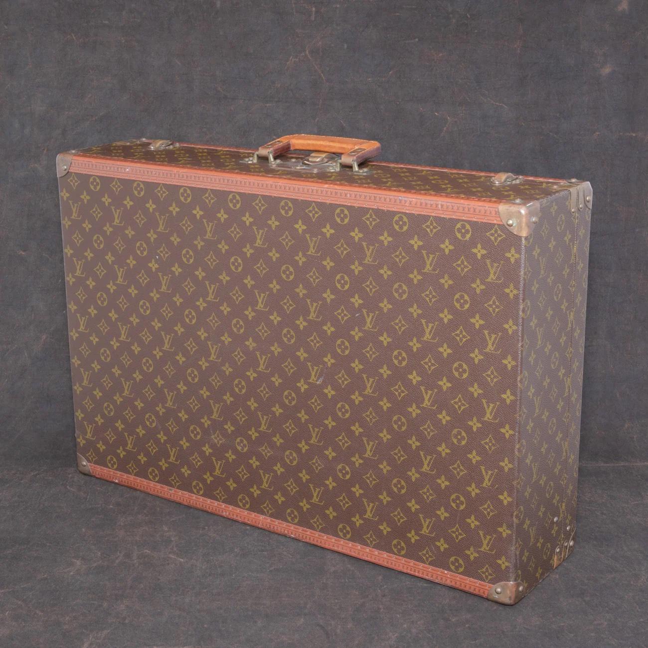 Louis Vuitton large ‘Fly-el’ suitcase in LV monogram pattern coated canvas with edges trimmed in lozine, a layered leather flat handle and unpolished brass fittings.

Securing the lid of the case is a central sprung catch with a lock, accompanied by