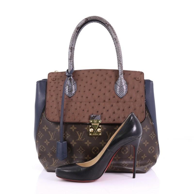 This Louis Vuitton Majestueux Tote Monogram Canvas and Exotics MM, crafted in brown monogram coated canvas and blue and brown exotics, features an angular silhouette, dual rolled handles, protective base studs, and gold-tone hardware. Its S-lock and
