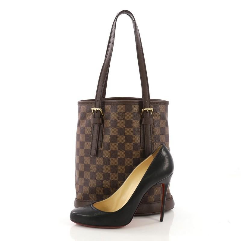 This Louis Vuitton Marais Bucket Bag Damier, crafted from damier ebene coated canvas, features dual tall leather handles with buckle details, brown leather trim, and gold-tone hardware. It opens to an orange microfiber interior with side zip