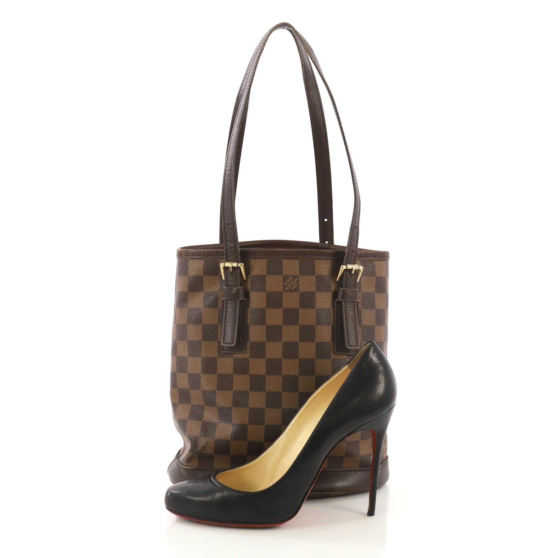This Louis Vuitton Marais Bucket Bag Damier, crafted from damier ebene coated canvas, features dual tall leather handles with buckle details, leather trim, and gold-tone hardware. It opens to an orange microfiber interior with side zip pockets.