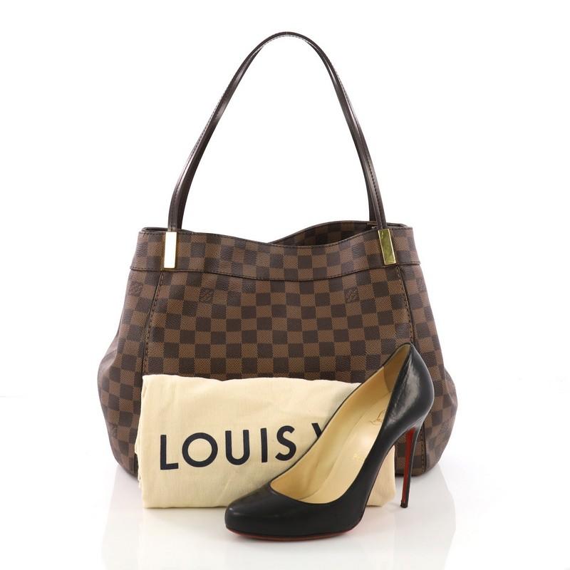 This Louis Vuitton Marylebone Handbag Damier GM, crafted from damier ebene coated canvas, features dual flat handles, gold bar accents, gusseted sides with snap closures, protective base studs, and gold-tone hardware. Its hook closure opens to a