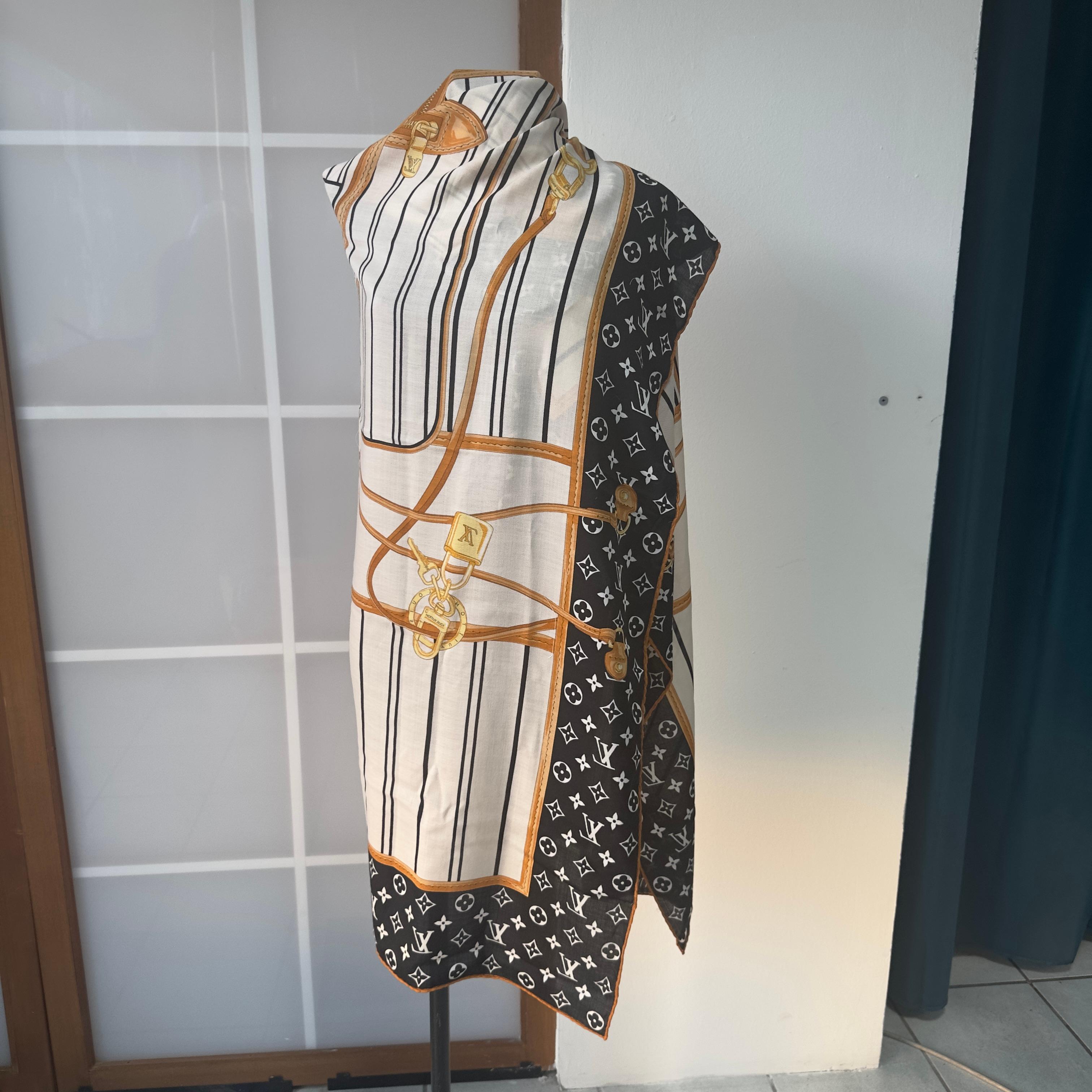 Un auténtico homenaje a la historia de la Maison Louis Vuitton.
Este canesú de seda brillante presenta un imponente estampado central que reproduce la silueta de una maleta de viaje vintage, enmarcada por el clásico motivo Monogram sobre fondo negro