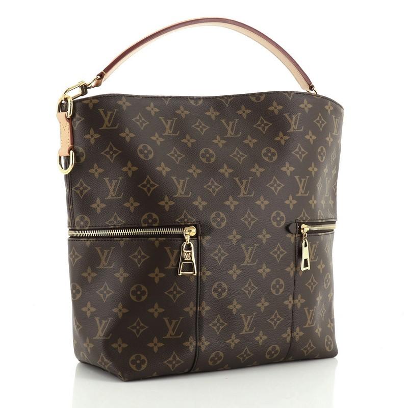 This Louis Vuitton Melie Handbag Monogram Canvas, crafted in brown monogram coated canvas, features a single looped leather handle, two exterior side zip pockets, and gold-tone hardware. It opens to a purple microfiber interior with slip pockets.