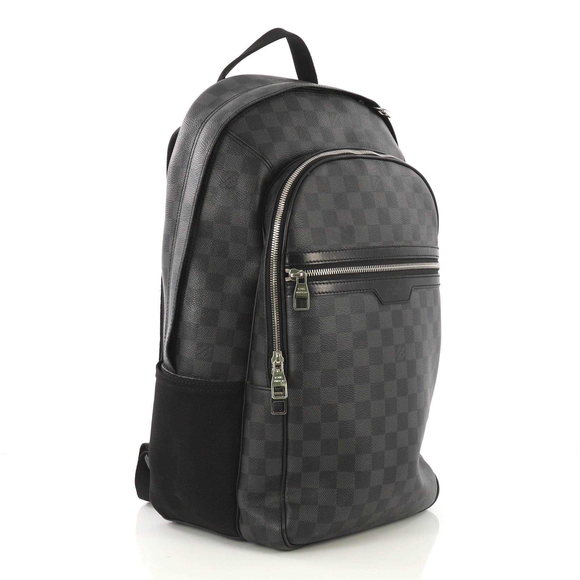 This Louis Vuitton Michael Backpack Damier Graphite, crafted from damier graphite coated canvas and black leather, features top leather handle, canvas padded backpack straps, leather trim, two exterior front zip pockets, and silver-tone hardware.