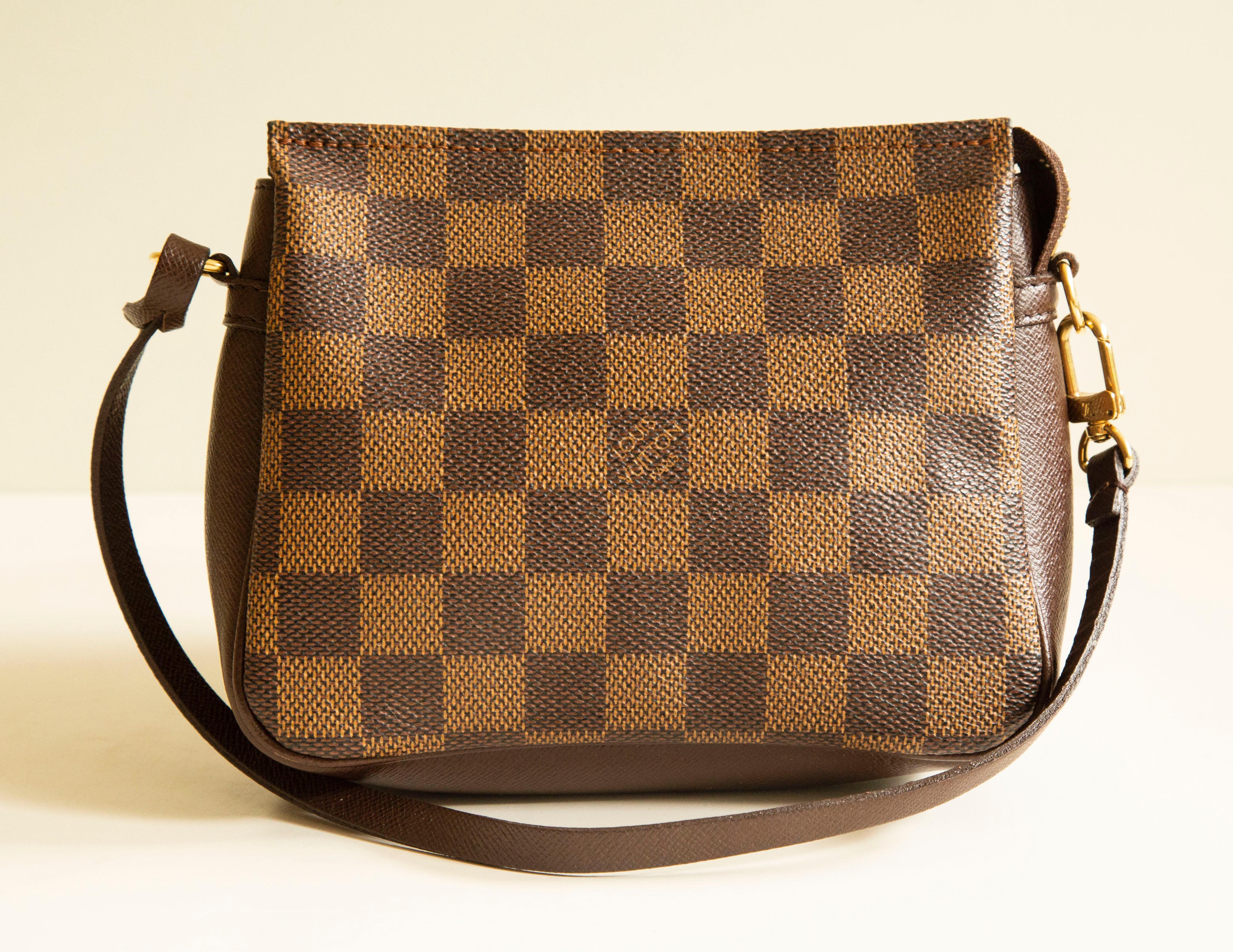 A Louis Vuitton Mini Trousse (evening) clutch or to be used as a daily accessory from the 1998 Collection by Marc Jacobs. The bag is made of brown leather and coated canvas in Damier Ebene with gold toned hardware. The interior is lined with red