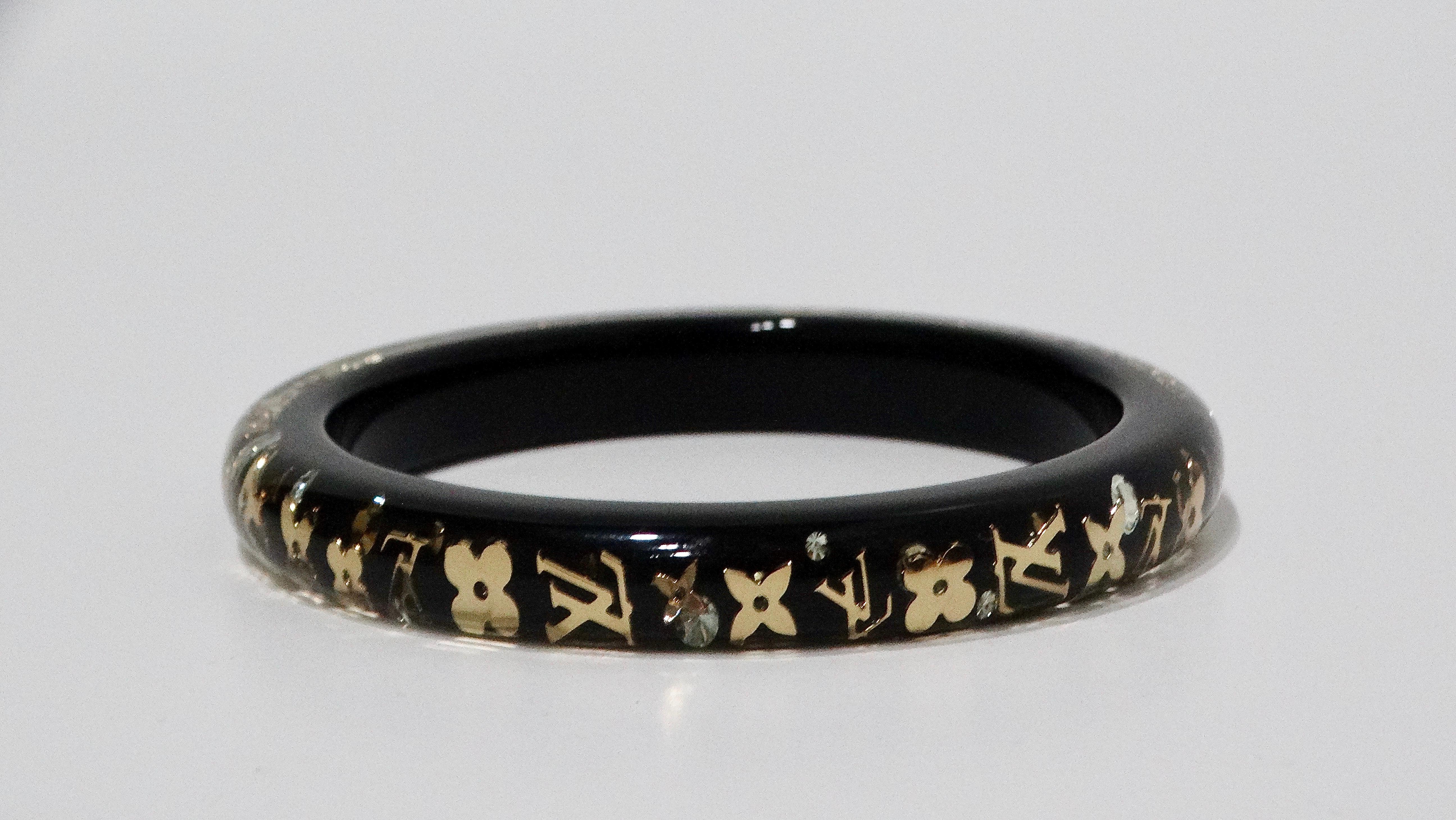 The Louis Vuitton black resin bangle with lucite is an exquisite accessory that seamlessly combines elegance and modern style. Adorned with gold-toned iconic LV monogram emblems and sparkling rhinestones, this bangle adds a touch of luxury and