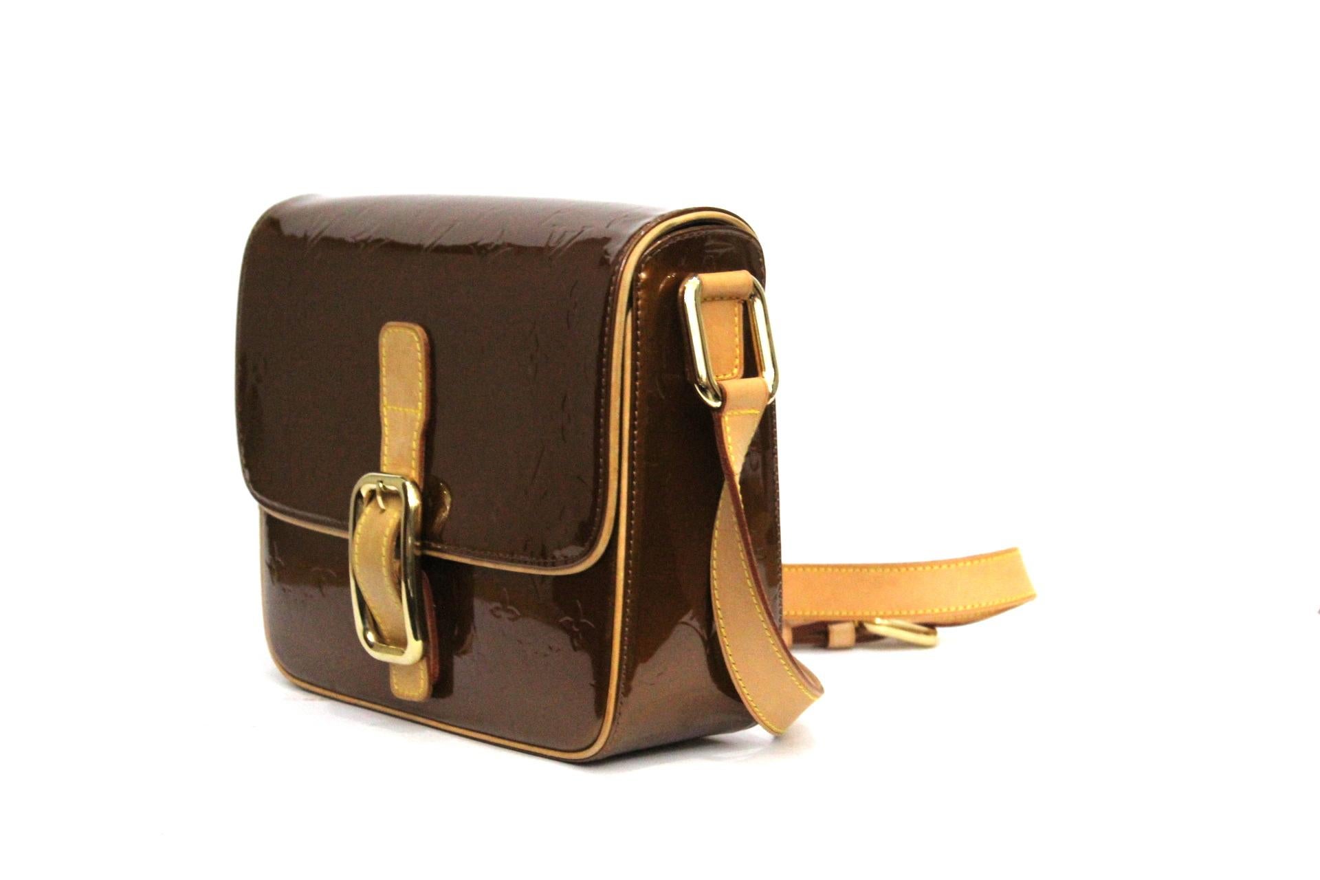 Striking Vernis leather, flap top with buckle and strap closure, gold tone hardware, cowhide leather trimming and adjustable shoulder strap currently set at 20-inch drop. A slip-in pocket on the back. Man made brown leather lining inside with one