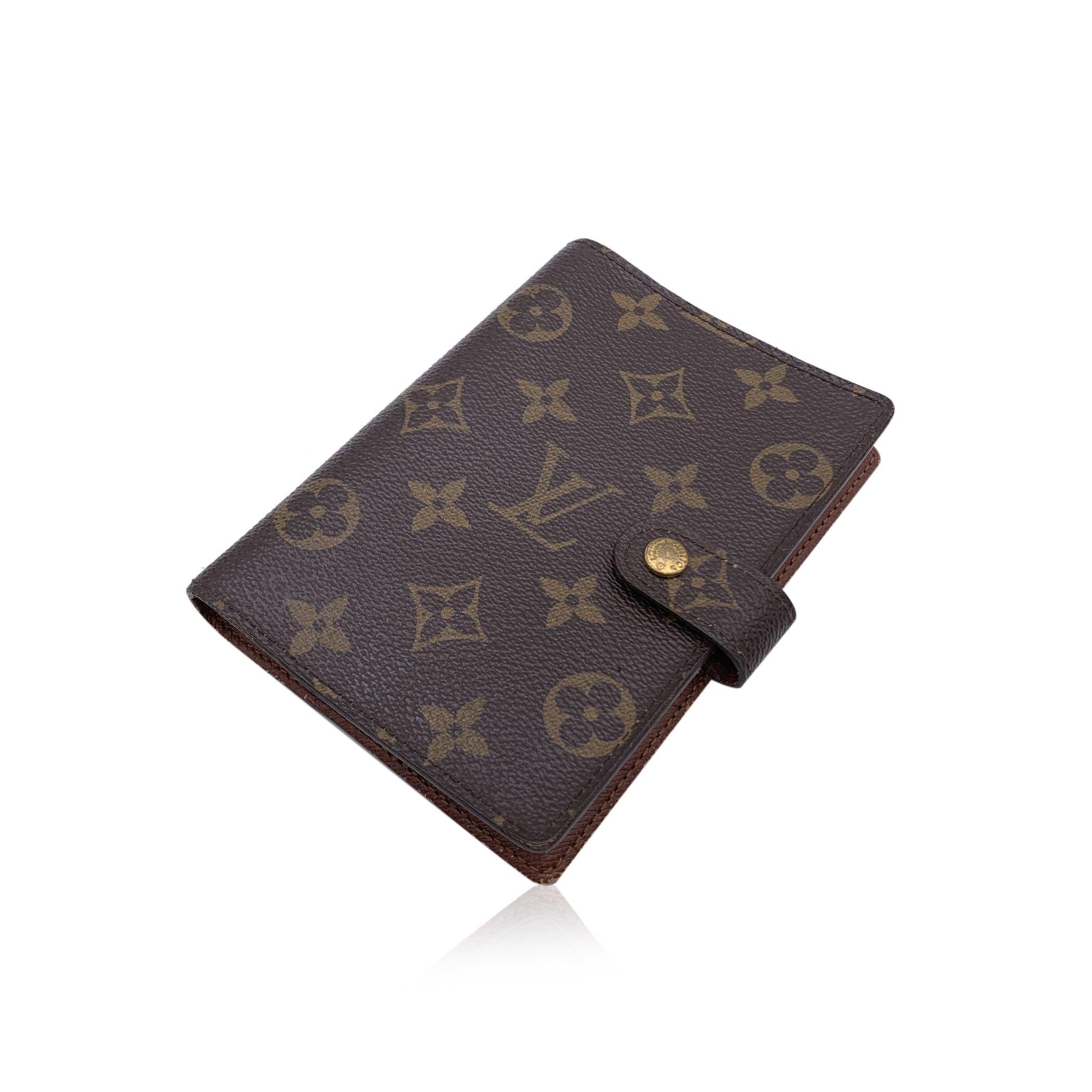 Agenda cover in brown Monogram canvas by LOUIS VUITTON. Press stud closure. Brown leather interior. Six- Ring binder. 1 pen holder. 3 credit card slots. 2 side sleeve for papers. Authenticity serial number embossed inside. 'Louis Vuitton - made in