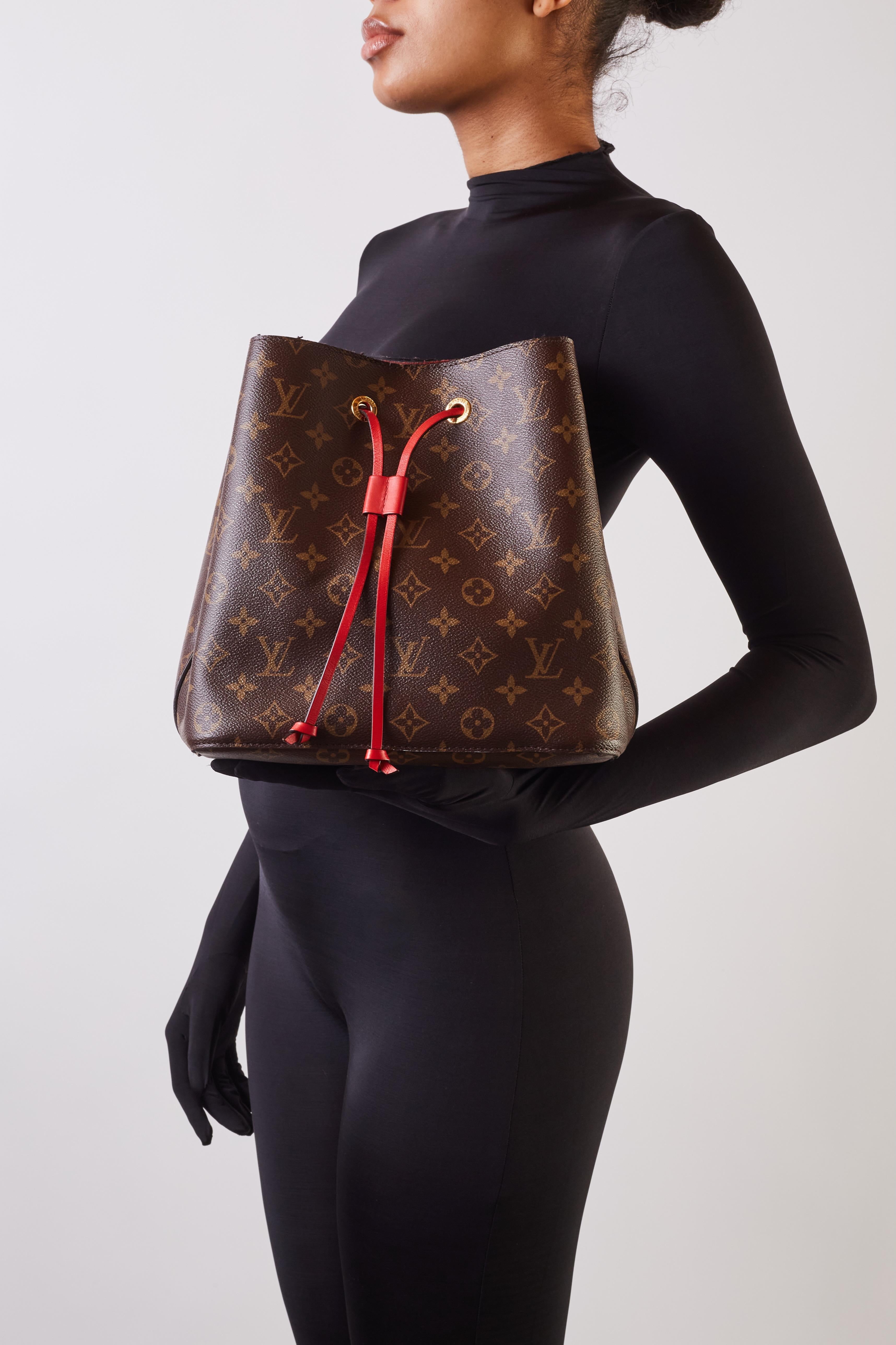 El bolso está confeccionado con lona estampada con monograma y acabados en piel roja. El bolso tiene un cordón de cuero rojo con cierre de broche, una correa ajustable para el hombro y herrajes dorados. La bolsa está acabada con un interior de