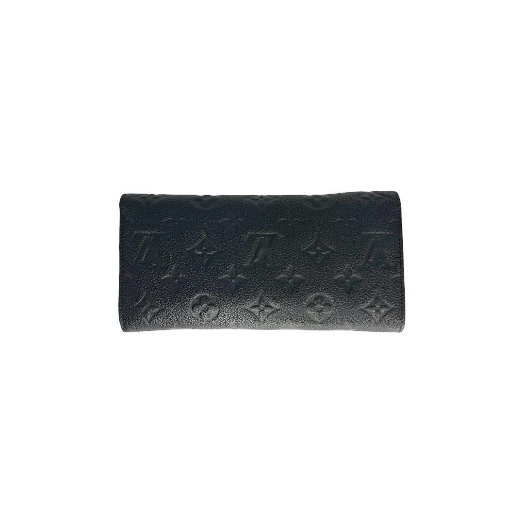 This Louis Vuitton envelope-style wallet was made in Spain from 2014 and it is finely crafted of a black Louis Vuitton Empreinte Leather exterior with gold-tone hardware features. It has a fold over snap closure that opens up to a black leather