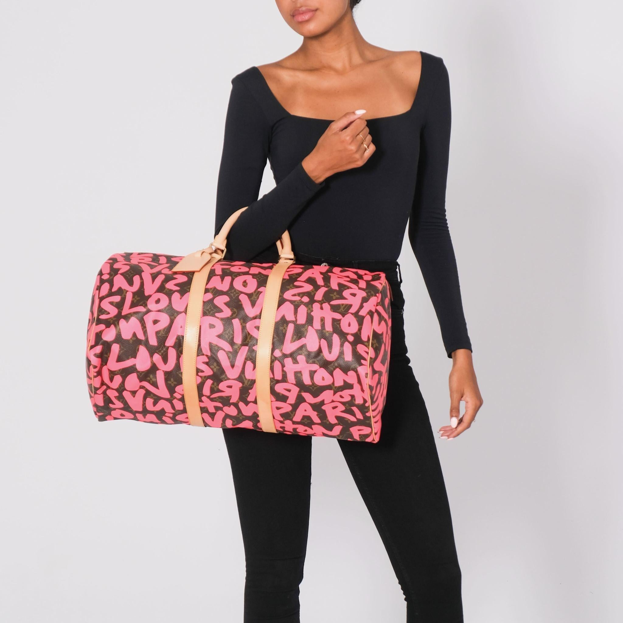 This bag is made of classic Louis Vuitton monogram on coated canvas, with a fuchsia graffiti overlay. The bag features natural vachetta leather rolled top handles and trim, with polished brass hardware. The double top zippers open to a spacious
