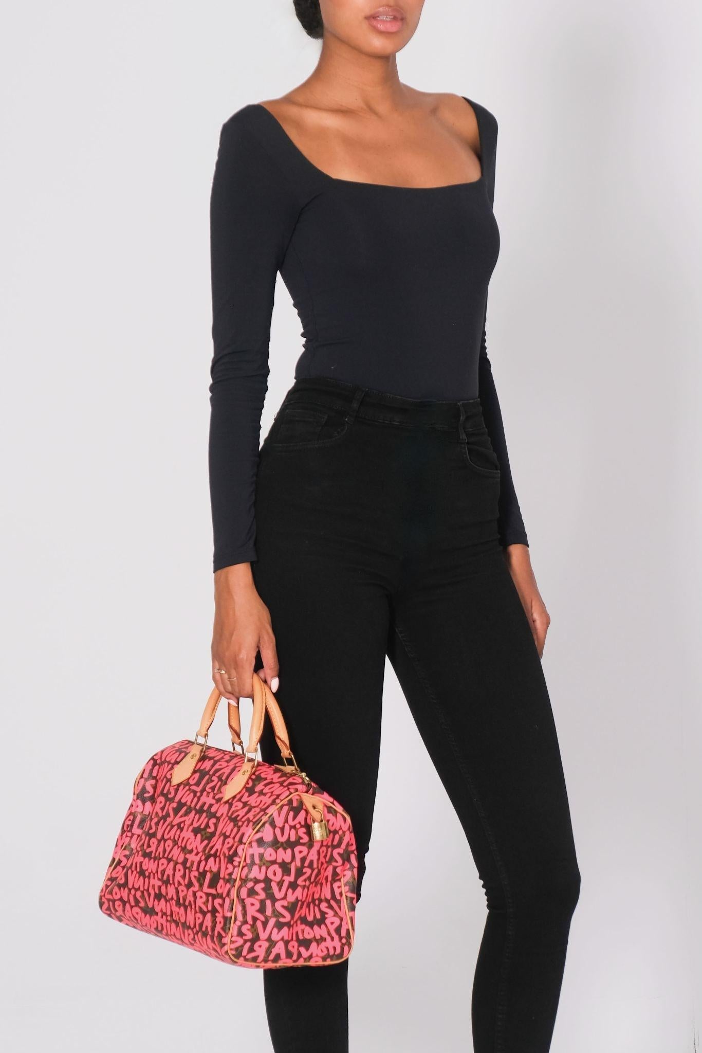This bag is made of classic Louis Vuitton monogram on coated canvas, with a fuchsia graffiti overlay. The bag features natural vachetta leather rolled top handles and trim, with polished brass hardware. The double top zippers open to a spacious