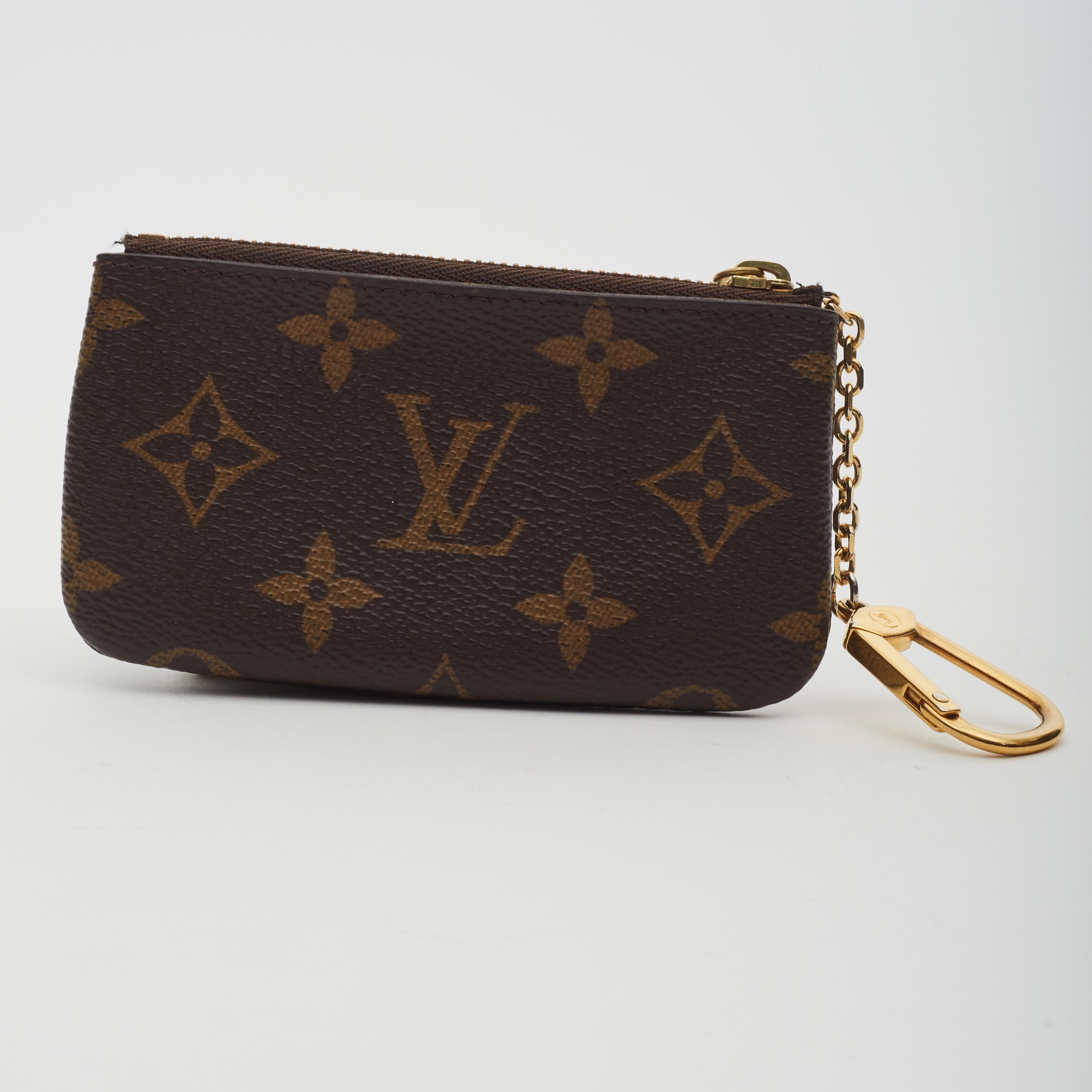 The holder is a small pouch of classic Louis Vuitton monogram on toile canvas with a brass top zipper. This opens to a brown cross-grained leather interior with a D-ring clasp.

Color: Brown monogram print
Material: Coated canvas with vachetta