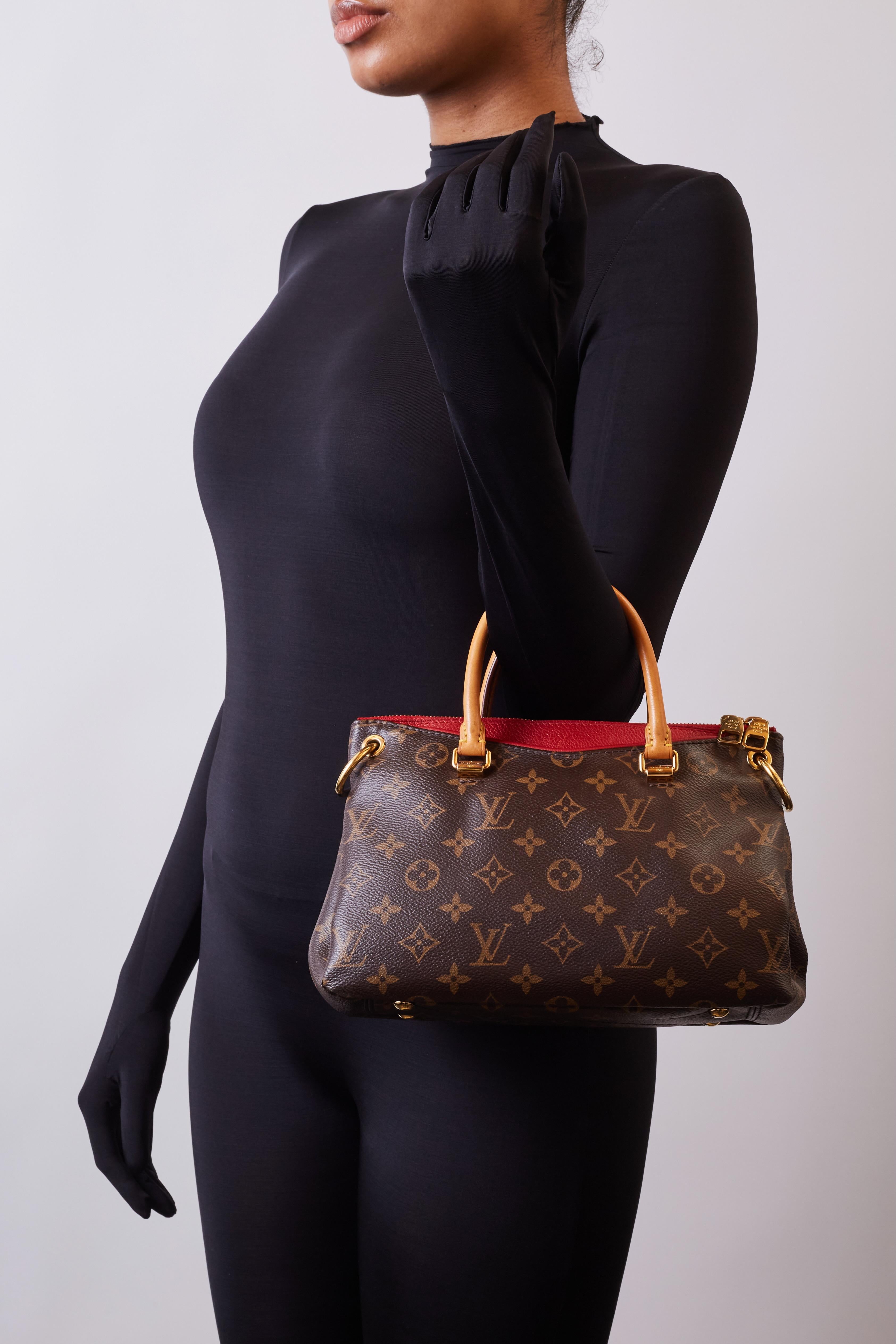 This bag is composed of the signature LV monogram coated canvas. Contrast is provided in red (Cerise) leather details throughout. The bag features gold-tone hardware, cowhide (Vachetta) trim, yellow contrast-stitching, 4 protective metal feet at