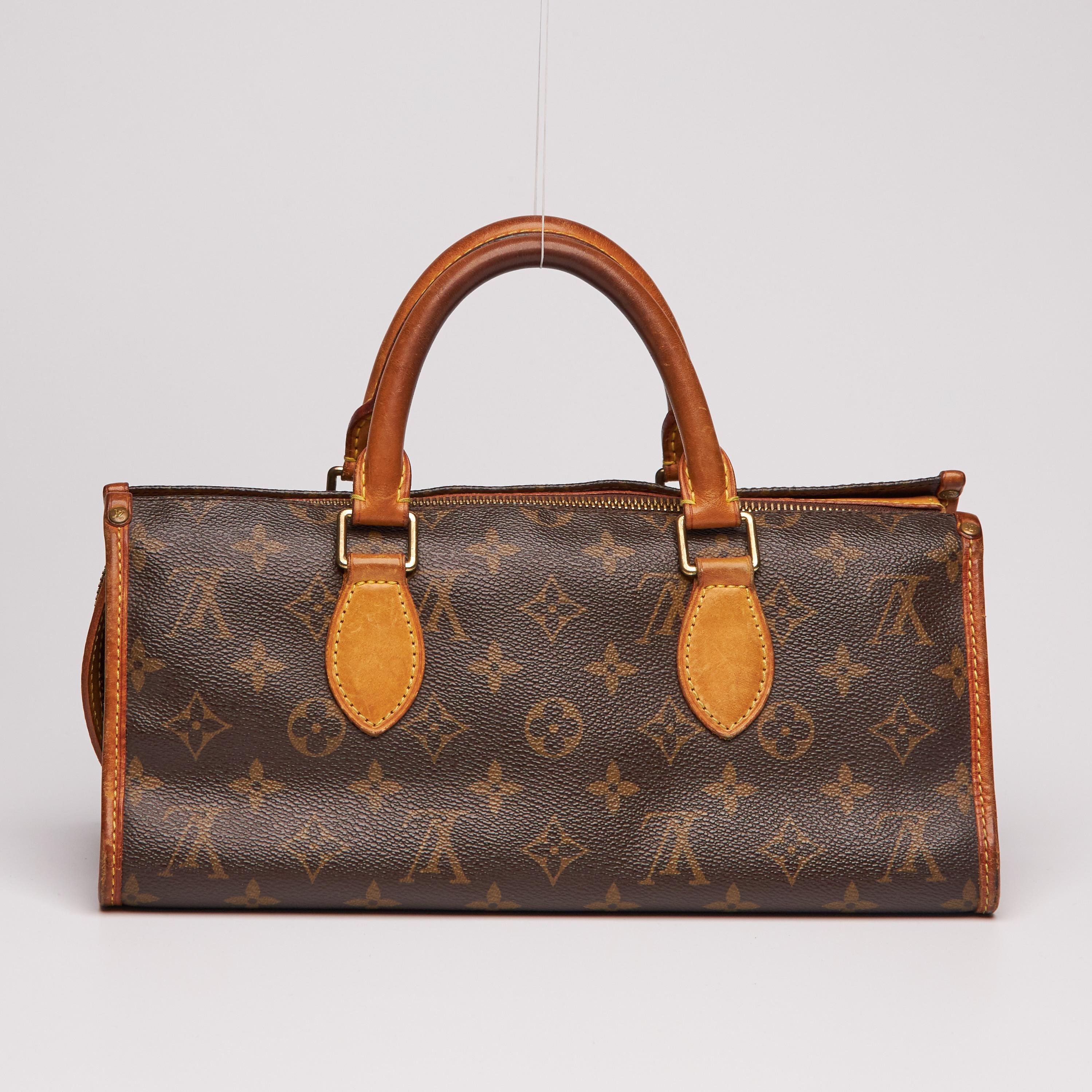 
The triangle shaped handbag is constructed of traditional Louis Vuitton monogram coated canvas trimmed with vachetta cowhide leather at the side edges and smooth rolled leather top handles. The bag has brass hardware including an overextended brass