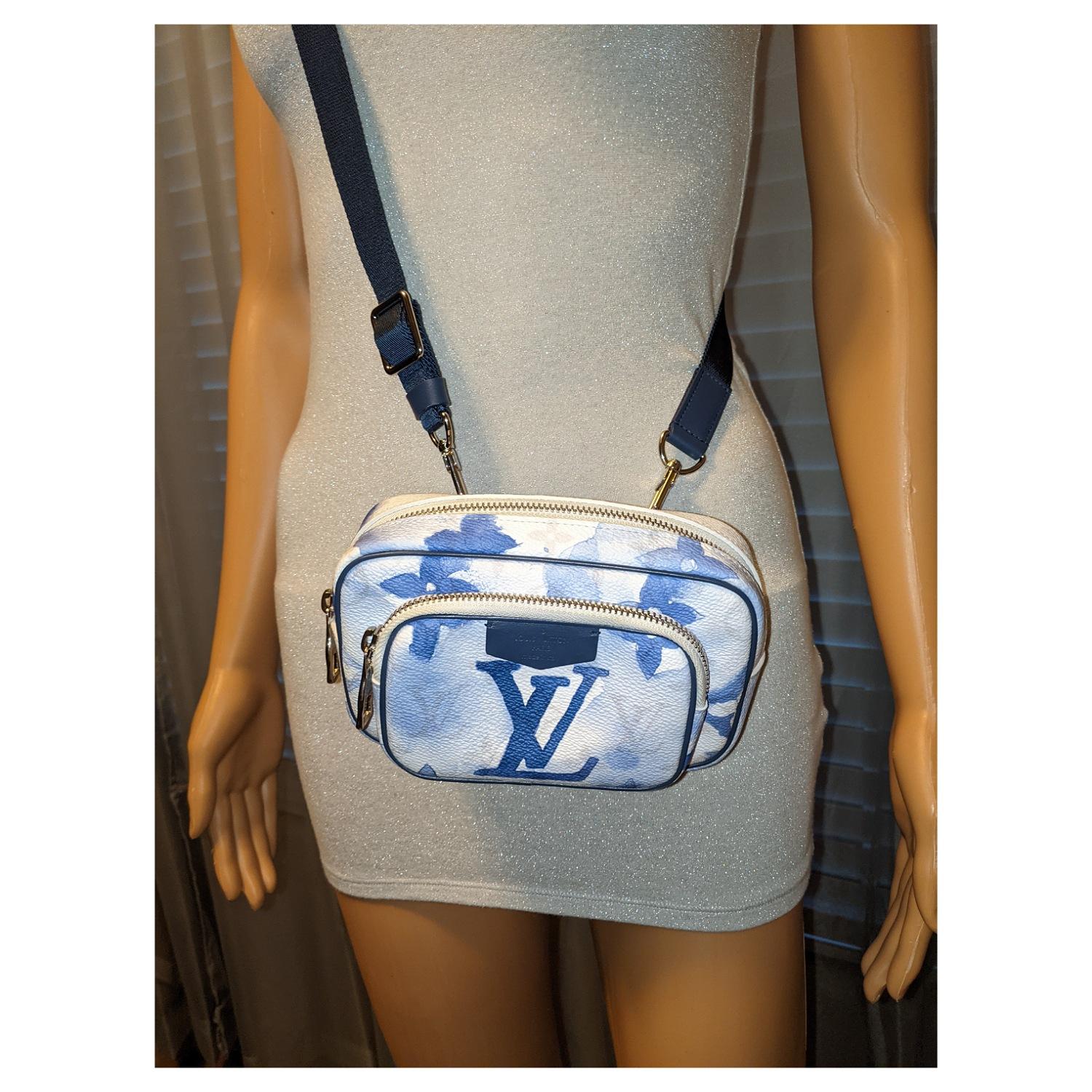 This stylish bag is crafted of Monogram canvas in white with a blue watercolor effect. The bag features a blue fabric adjustable shoulder strap and a front zipper pocket. The top zipper opens to a blue fabric interior with a patch pocket.