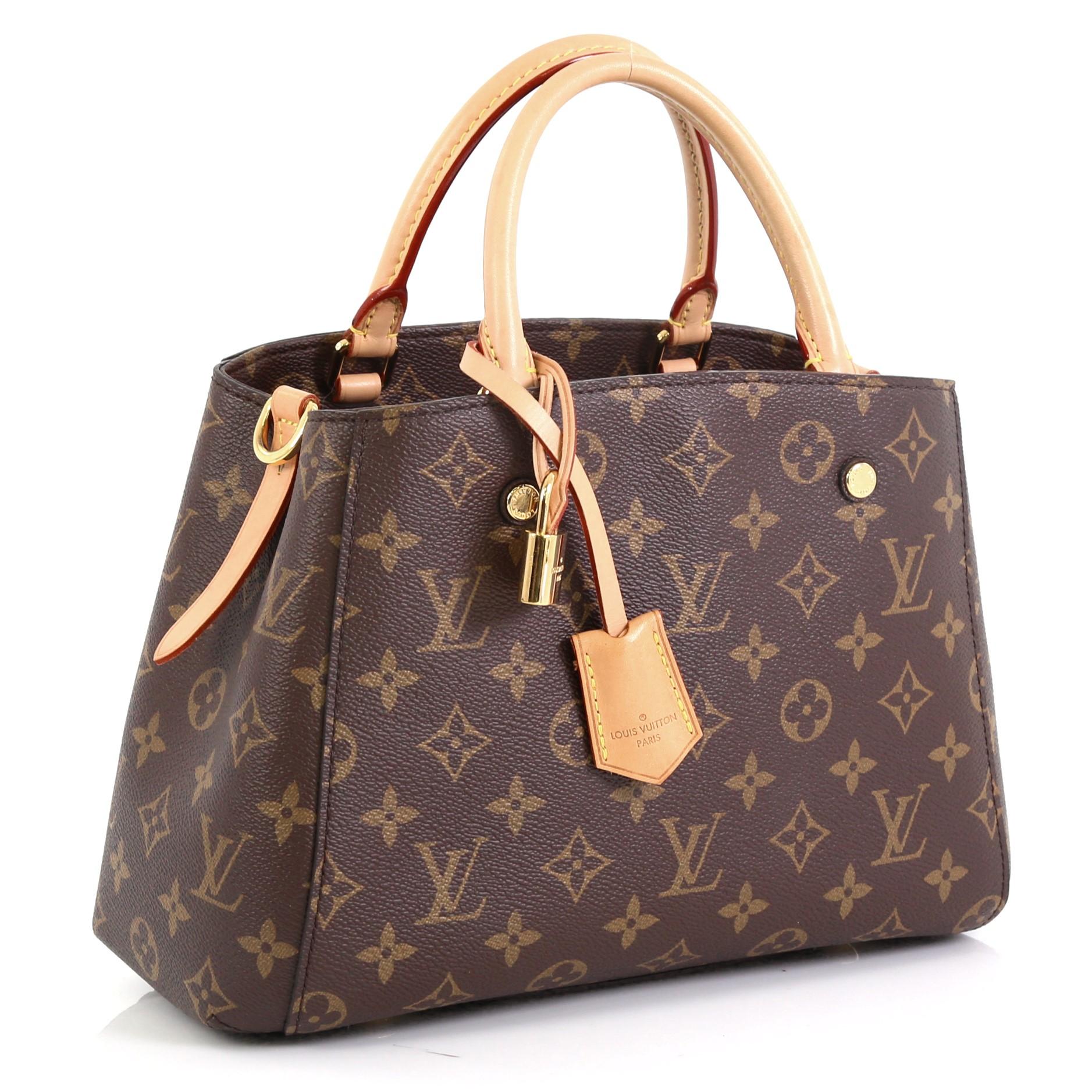 This Louis Vuitton Montaigne Handbag Monogram Canvas BB, crafted in brown monogram coated canvas, features dual rolled vachetta leather handles, protective base studs, and gold-tone hardware. Its hook closure opens to a purple microfiber interior
