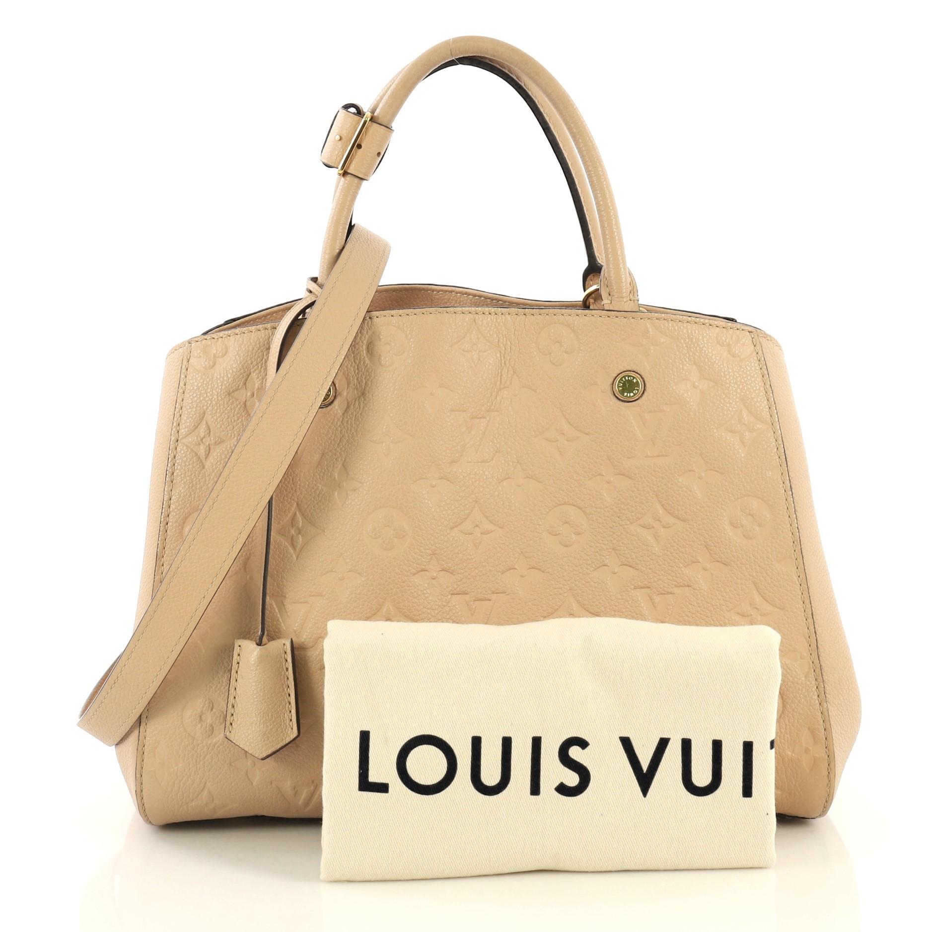This Louis Vuitton Montaigne Handbag Monogram Empreinte Leather MM, crafted in neutral monogram empreinte leather, features dual rolled leather handles, protective base studs, and gold-tone hardware. Its hook closure opens to a neutral fabric