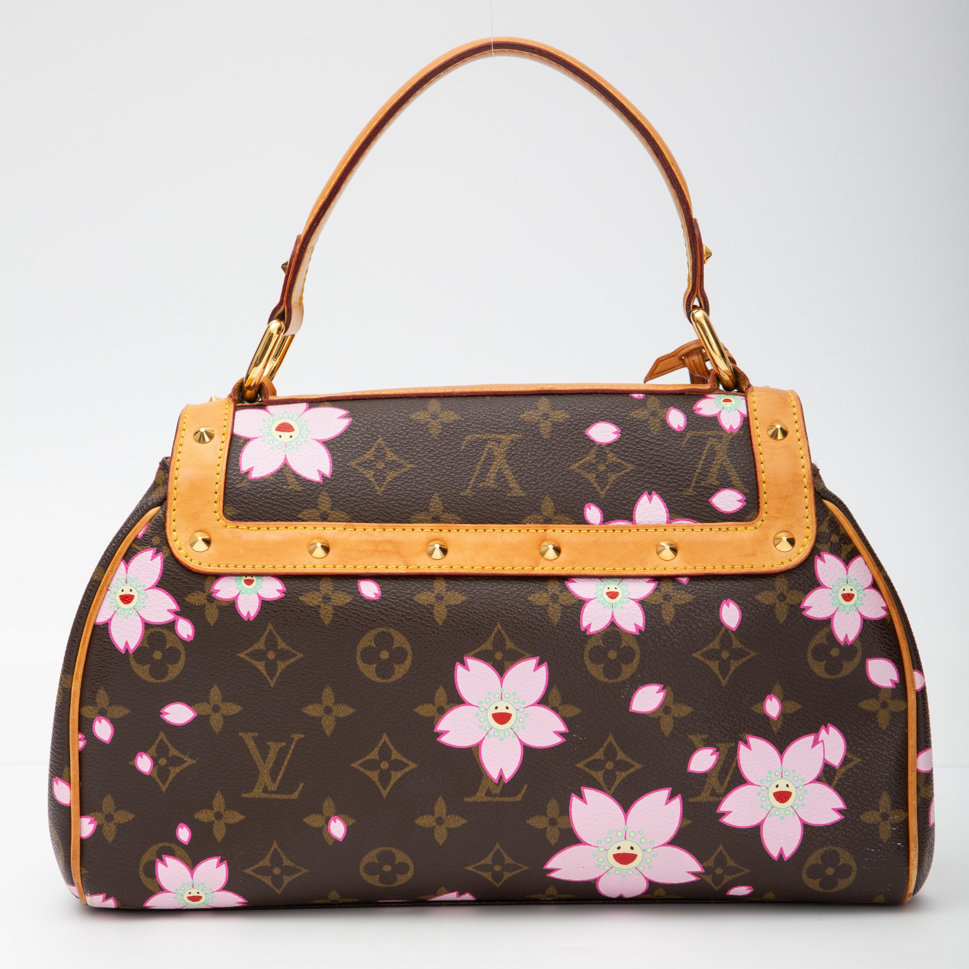 This handbag is made of classic Louis Vuitton monogram, printed with artwork by Takashi Murakami of smiling cherry blossom faces on coated canvas. This bag features pyramid cone studs, a vachetta leather top handle and a flap closure with a bow.