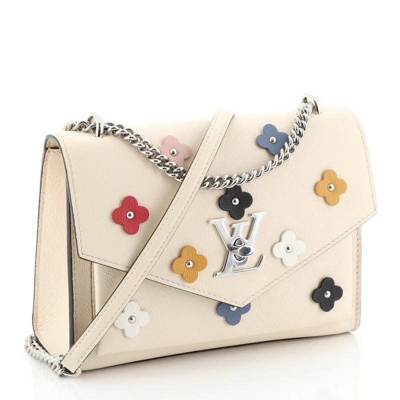 This Louis Vuitton Mylockme Handbag Flower Embellished Leather BB, crafted in neutral flower embellished leather, features chain link strap with leather pad, exterior back zip pocket, slip pocket under flap, and silver-tone hardware. Its LV