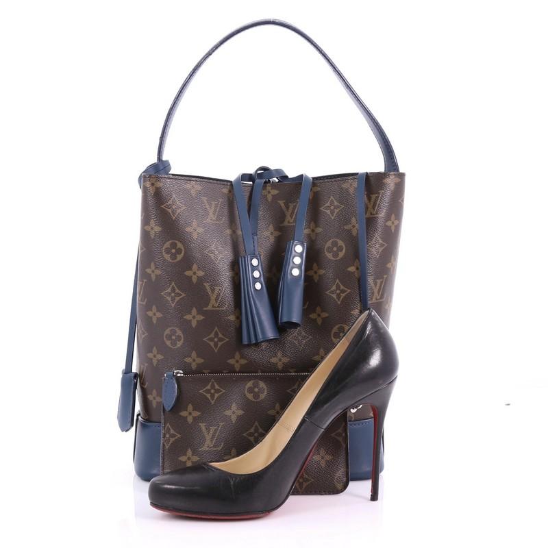 This Louis Vuitton NN14 Idole Bucket Bag Monogram Canvas and Leather GM, crafted from brown monogram coated canvas and blue leather, features hand-pleated leather tassels, flat handle, and silver-tone hardware. It opens to a blue microfiber
