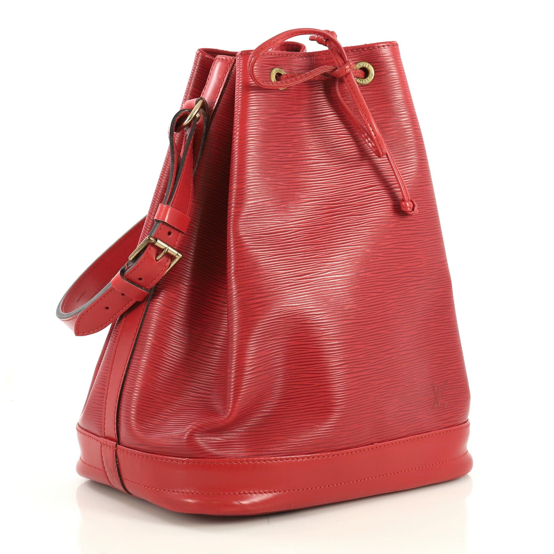 This Louis Vuitton Noe Handbag Epi Leather Large, crafted in red epi leather, features an adjustable shoulder strap, leather drawstring threaded through metal eyelets, and gold-tone hardware. Its drawstring closure opens to a red microfiber interior