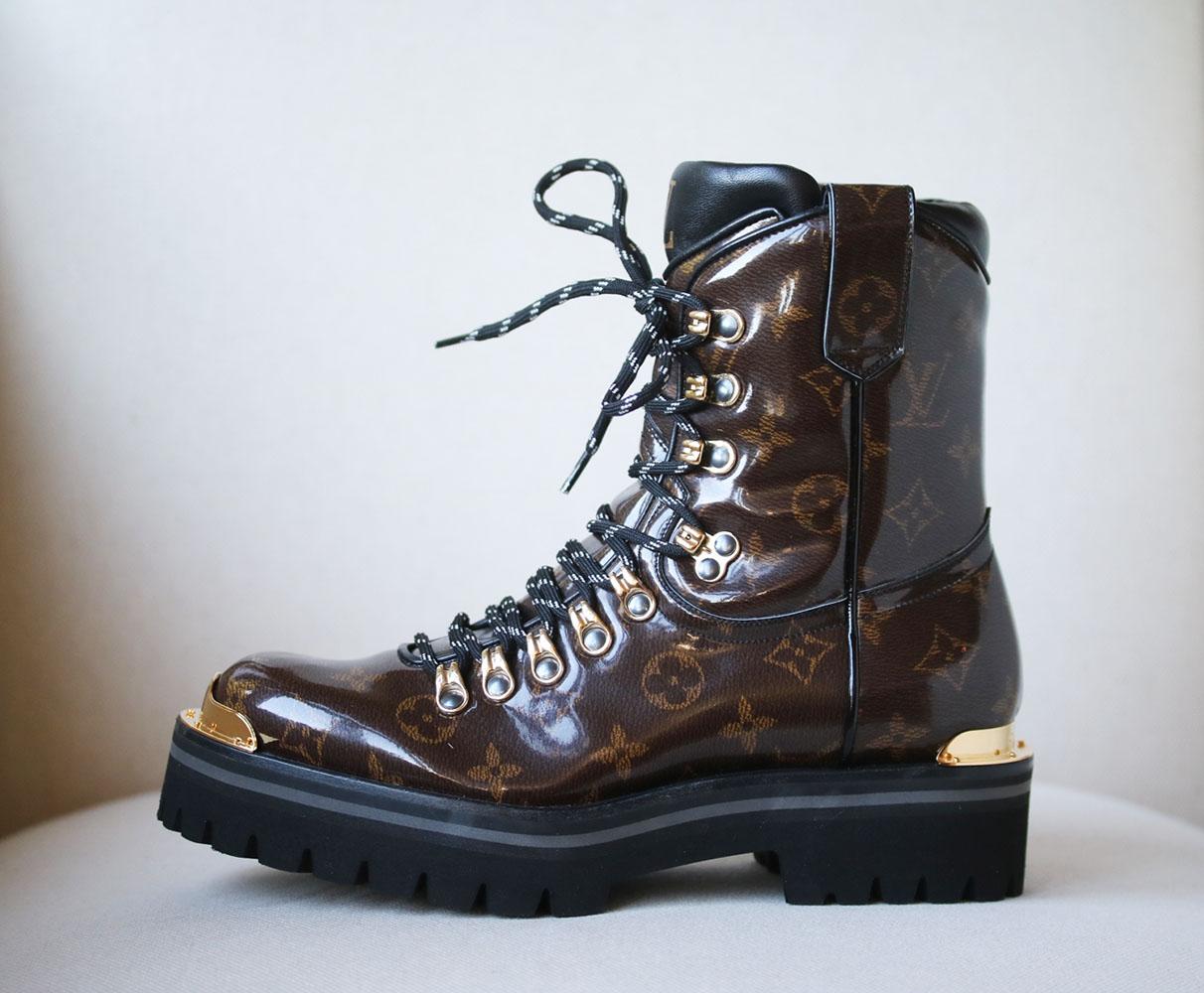 Unisex boots (mens sizing). Brown and tan glazed Monogram canvas Louis Vuitton Outland round-toe hiking boots. Gold-tone hardware. Rubber soles. Lace-tie closures at uppers. Round toe.  Upper: glazed canvas. Made in Italy. Does not come with a box. 