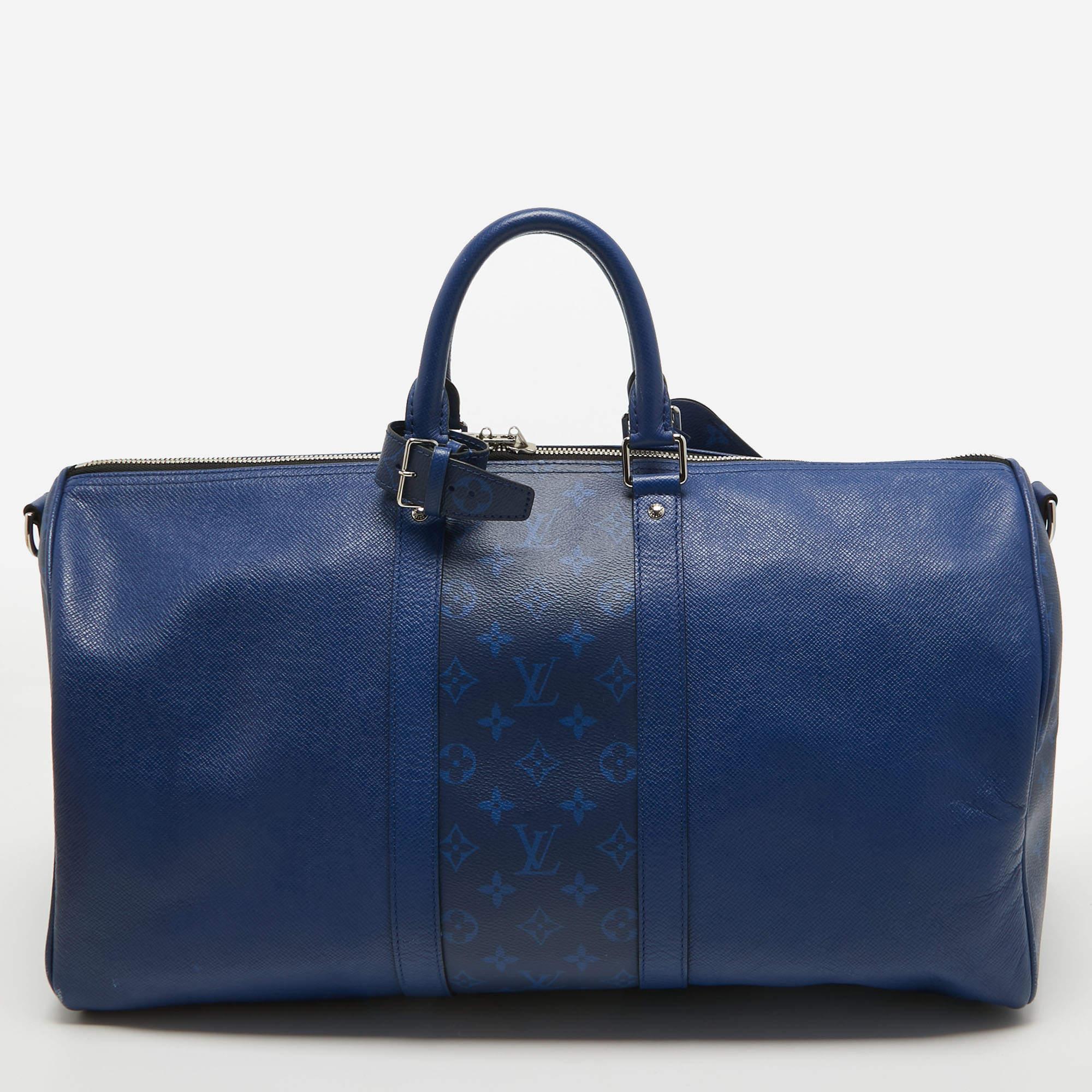 The Louis Vuitton Keepall Bandouliere 50 is a luxurious travel companion. Its exquisite design combines durable taiga leather in a striking Pacific Blue hue with the iconic Monogram Eclipse canvas. The spacious interior, reinforced leather handles,