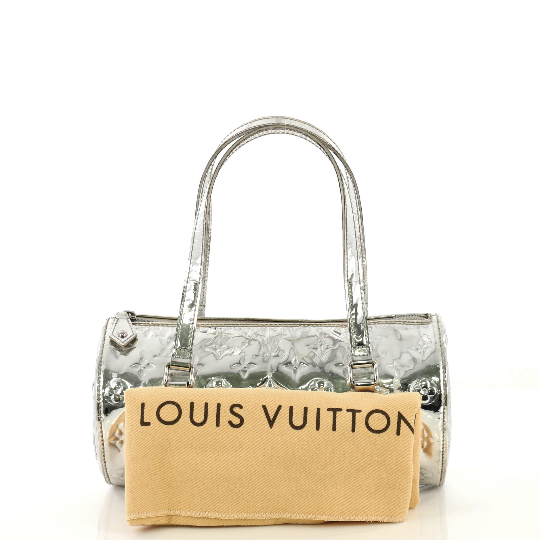 This Louis Vuitton Papillon Handbag Miroir PVC 26, crafted from silver miroir PVC, features dual flat handles, exterior side slip pocket, and silver-tone hardware. Its zip closure opens to a gray fabric interior. Authenticity code reads: MB1006.
