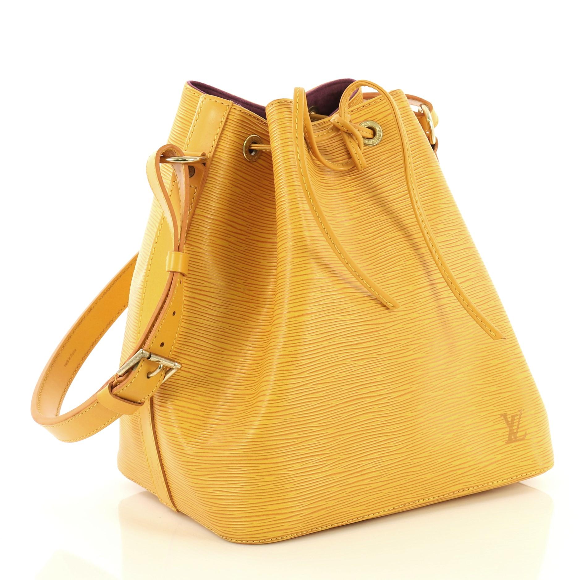 This Louis Vuitton Petit Noe Handbag Epi Leather, crafted in yellow epi leather, features adjustable shoulder strap, subtle LV logo, and gold-tone hardware. Its drawstring closure opens to a purple microfiber interior. Authenticity code reads: