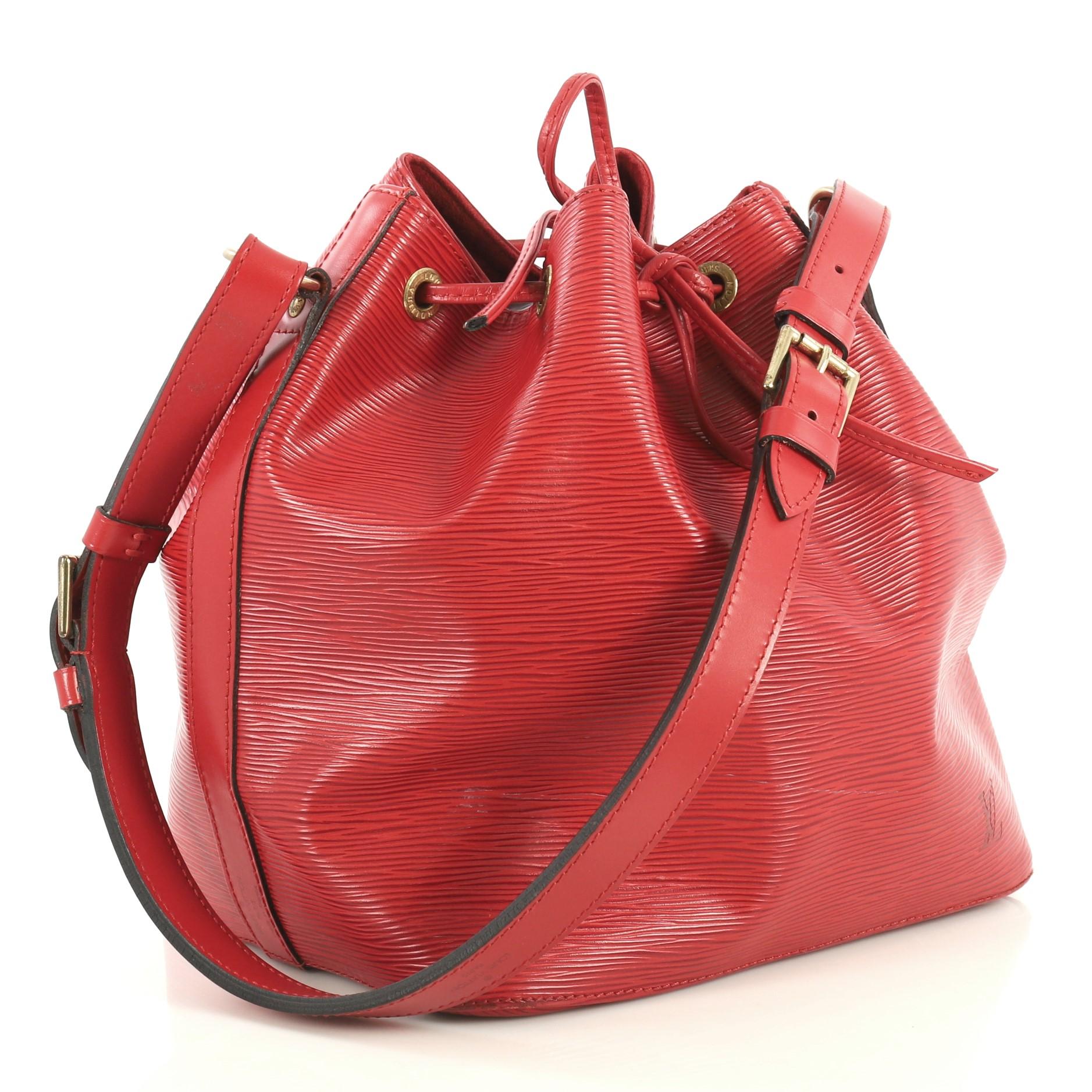 This Louis Vuitton Petit Noe Handbag Epi Leather, crafted in red epi leather, features an adjustable shoulder strap, subtle LV logo, and gold-tone hardware. Its drawstring closure opens to a red microfiber interior. Authenticity code reads: AR0925.