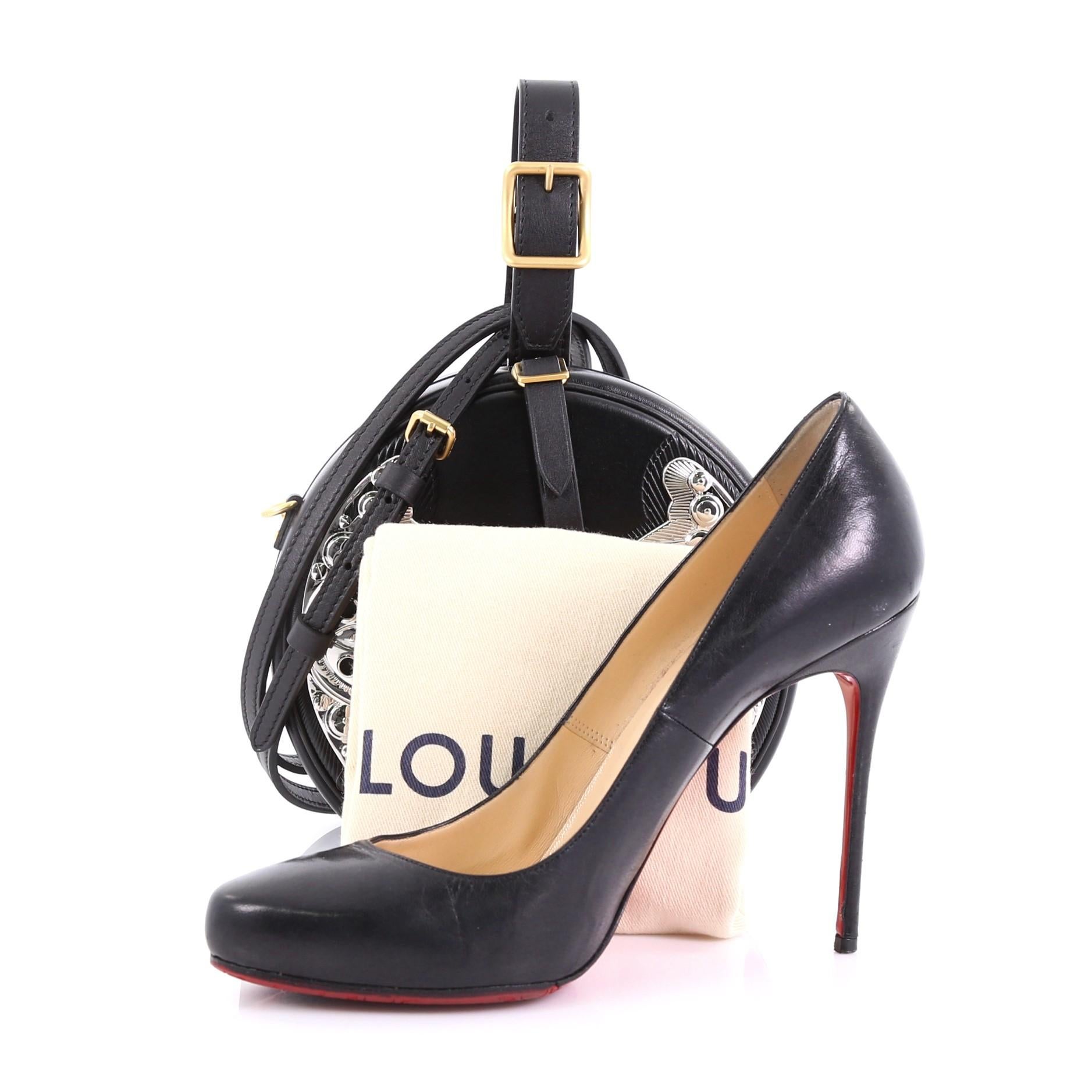 This Louis Vuitton Petite Boite Chapeau Bag Embellished Leather, crafted in black embellished leather, features an adjustable top leather handle, round silhouette, Wild West-inspired metallic design, and silver and matte gold-tone hardware. It opens