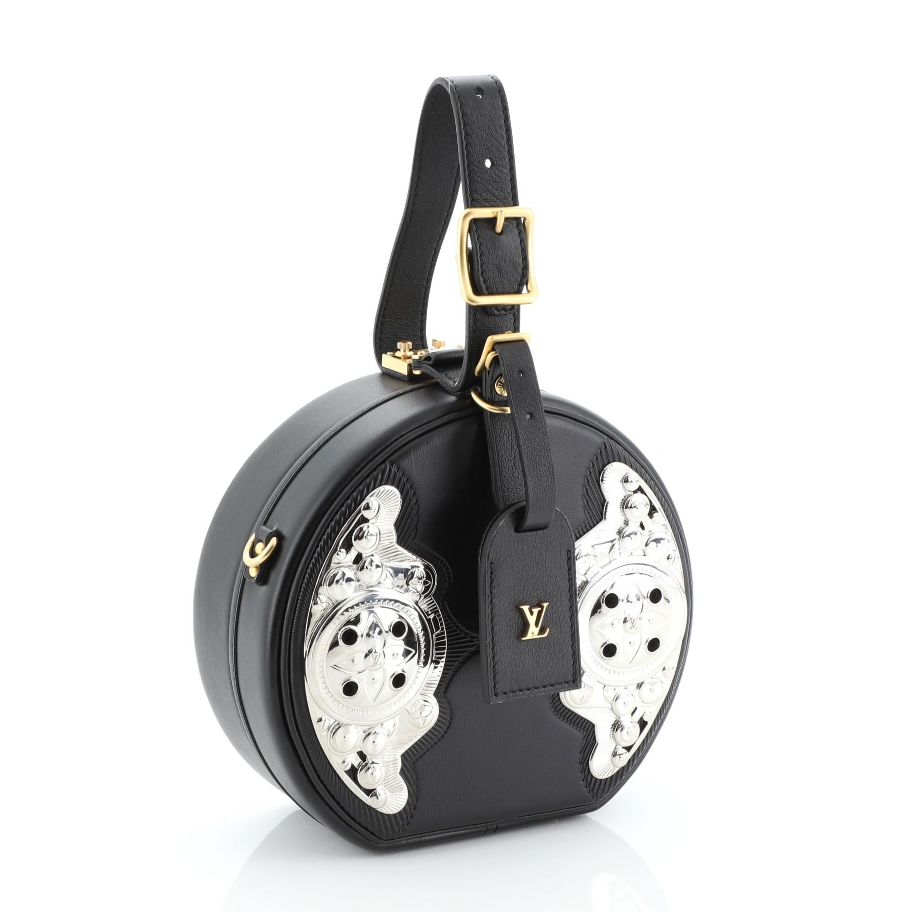 This Louis Vuitton Petite Boite Chapeau Bag Embellished Leather, crafted in black embellished leather, features an adjustable top leather handle, round silhouette, Wild West-inspired metallic design, and silver and gold-tone hardware. It opens to a
