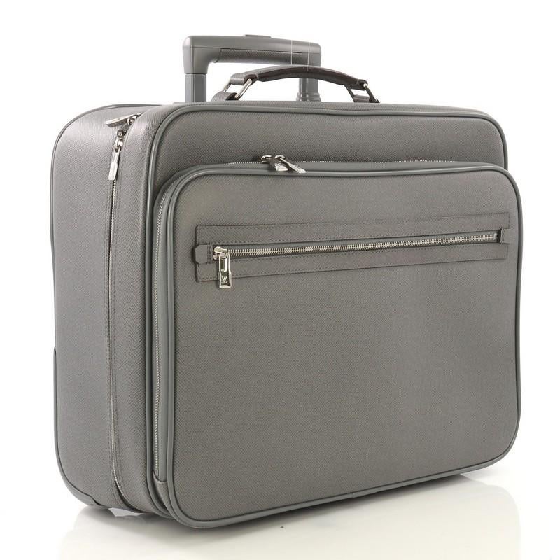 This Louis Vuitton Pilot Case Taiga Leather, crafted in gray taiga leather, features leather top handle, three-level telescopic handle with a lock-it button, wheels, exterior zip pocket, and compartment, and silver-tone hardware. Its two-way zip