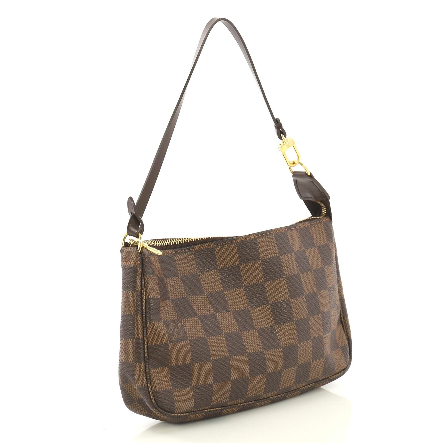 This Louis Vuitton Pochette Accessoires Damier, crafted from damier ebene coated canvas, features a flat leather strap and gold-tone hardware. Its zip closure opens to a red fabric interior. Authenticity code reads: CA1006. 

Estimated Retail Price: