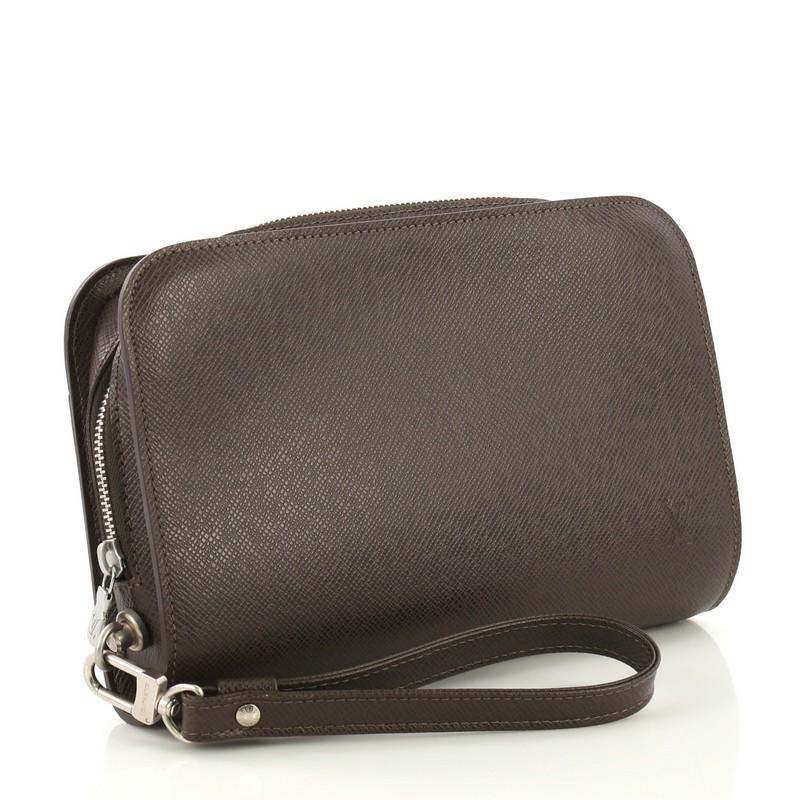 This Louis Vuitton Pochette Baikal Clutch Taiga Leather, crafted from brown taiga leather, features a detachable wristlet strap, exterior back slip pocket, subtle logo stamp, and silver-tone hardware. Its zip closure opens to a brown leather