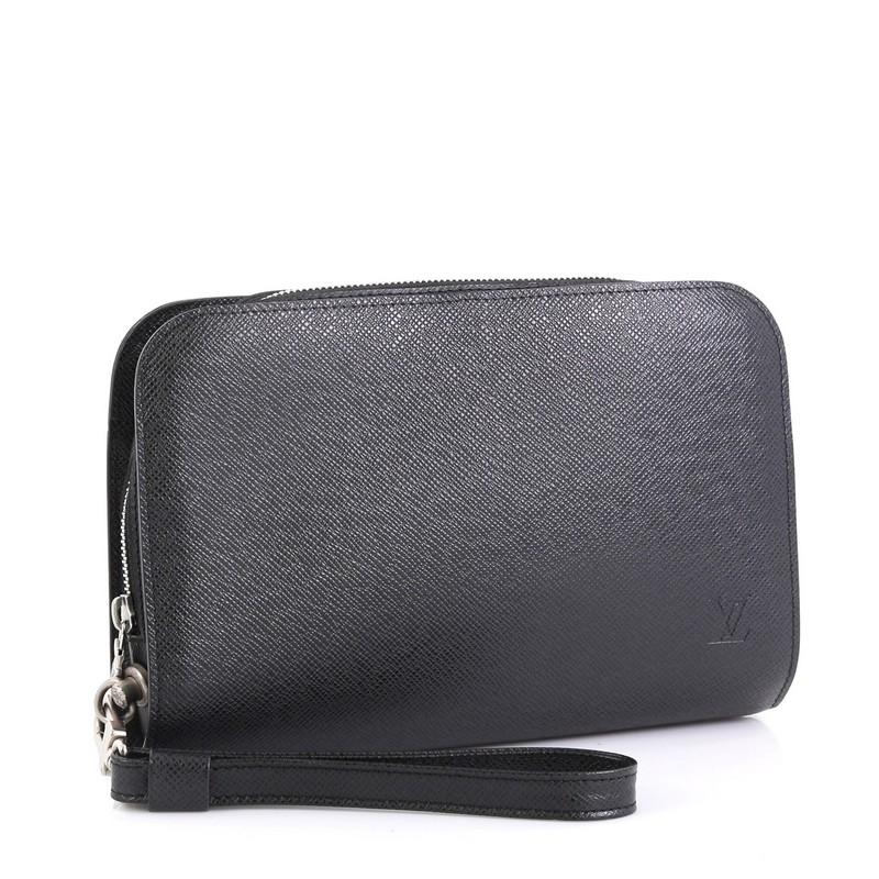 This Louis Vuitton Pochette Baikal Clutch Taiga Leather, crafted from gray taiga leather, features a detachable wristlet strap, exterior back slip pocket, subtle logo stamp, and silver-tone hardware. Its zip closure opens to a black leather interior