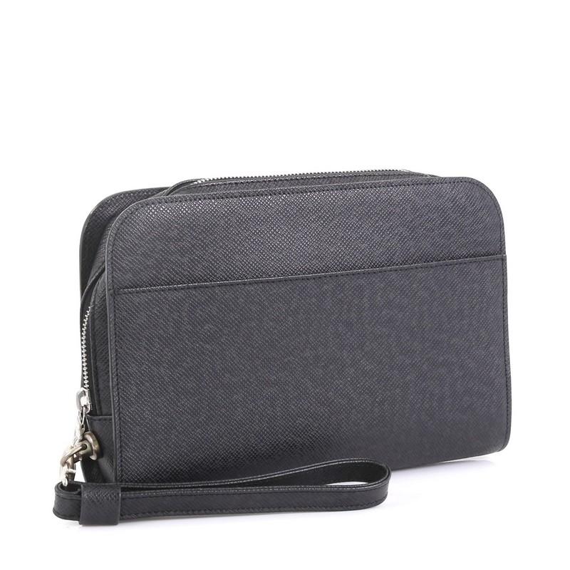 This Louis Vuitton Pochette Baikal Clutch Taiga Leather, crafted from black taiga leather, features a detachable wristlet strap, exterior back slip pocket, subtle logo stamp, and matte silver-tone hardware. Its zip closure opens to a black leather