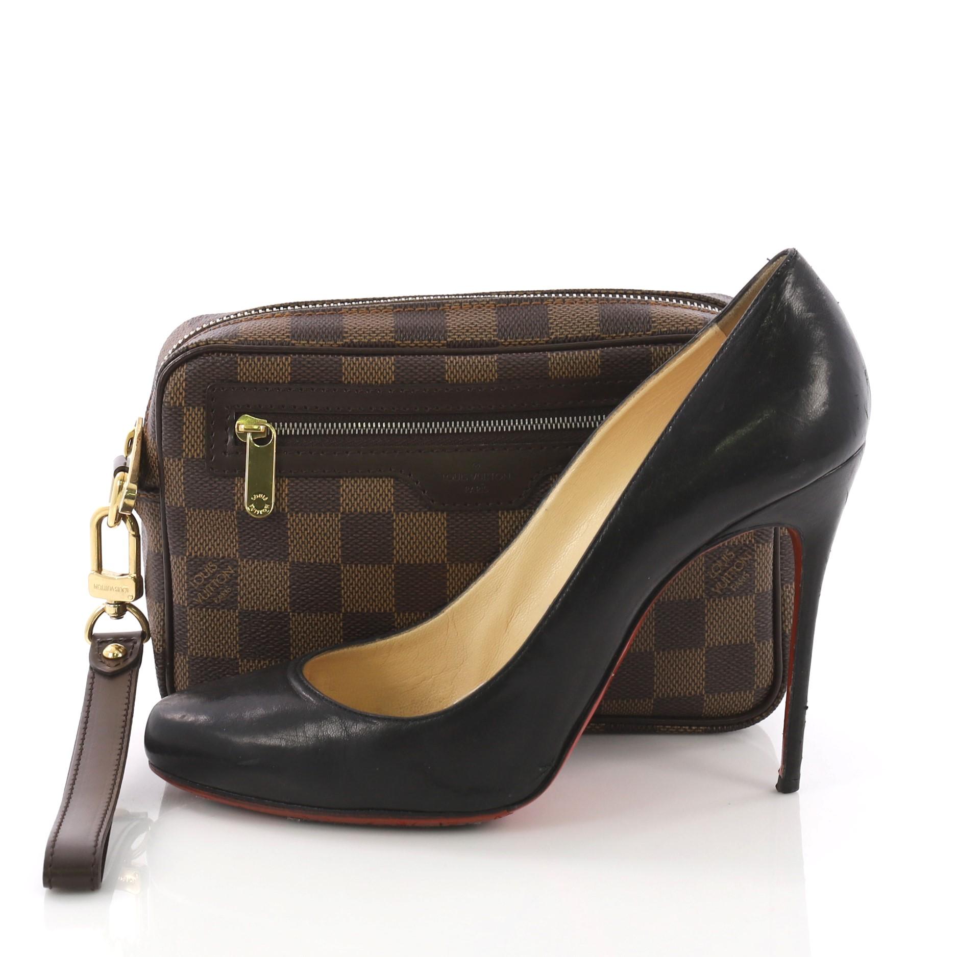 This Louis Vuitton Pochette Macao Damier, crafted in damier ebene coated canvas, features a wrist strap, dark brown leather trims, exterior front zip pocket and gold-tone hardware. Its zip closure open to a brown fabric interior with slip pockets.