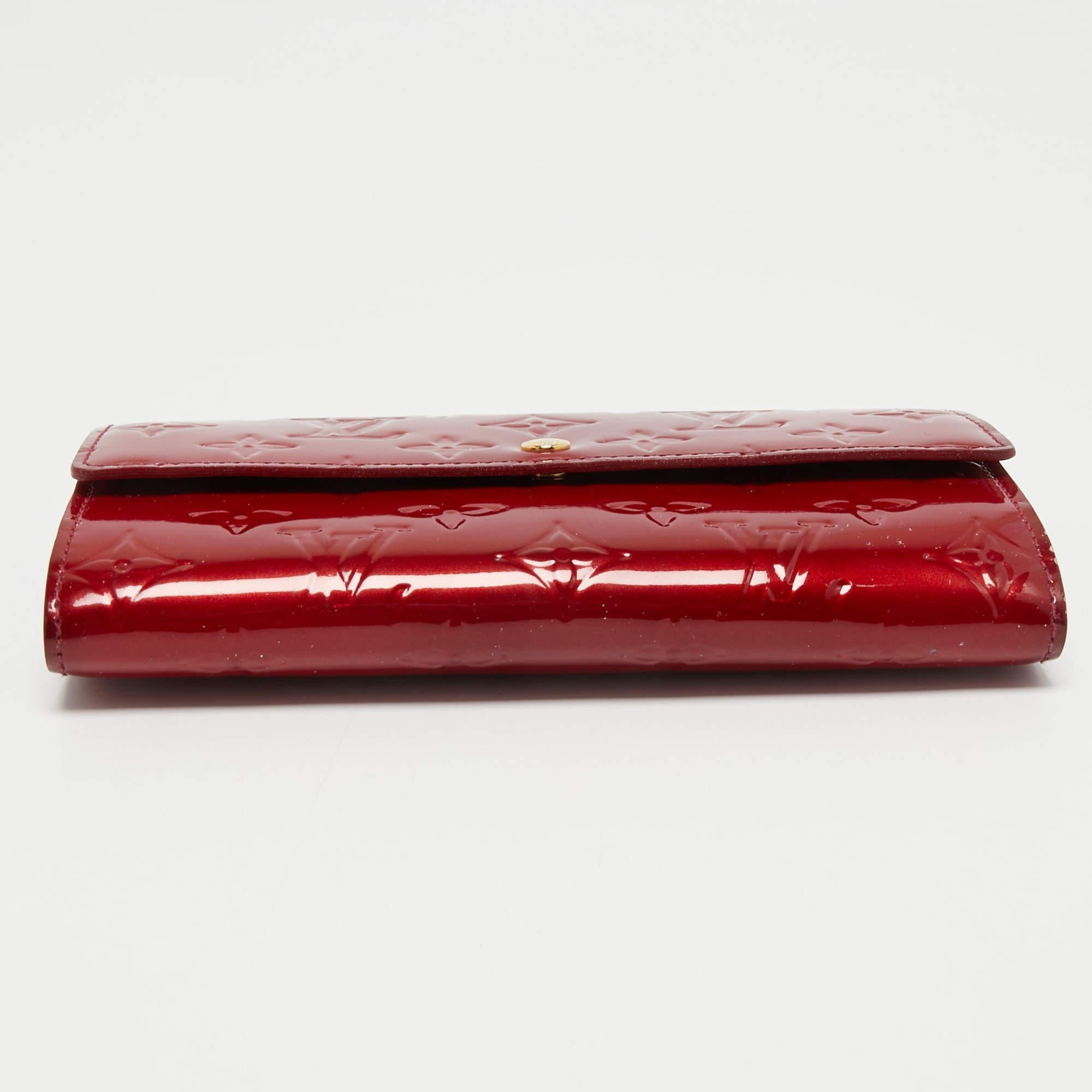 Eines der beliebtesten und bekanntesten Accessoires aus dem Hause Louis Vuitton ist dieses Sarah Portemonnaie. Sie wurde aus dem kultigen Leder Pomme D'amour Monogram Vernis gefertigt und weist auf der Vorderseite einen goldfarbenen Akzent auf. Er