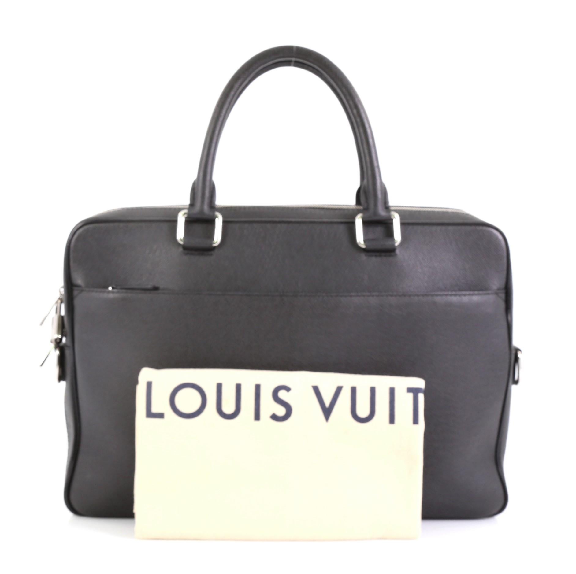 This Louis Vuitton Porte-Documents Business Bag Taiga Leather PM, crafted from black taiga leather, features dual rolled leather handles and silver-tone hardware. Its two-way zip closure opens to a black fabric interior with multiple slip pockets.