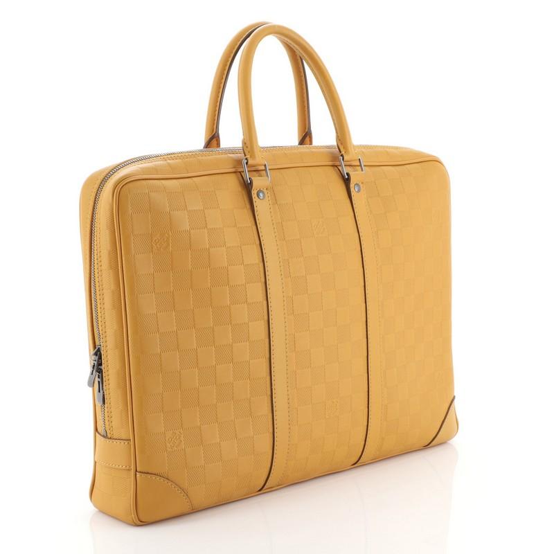This Louis Vuitton Porte-Documents Voyage Briefcase Damier Infini Leather, crafted in orange damier infini leather, features dual rolled handles, leather base corners, and aged silver-tone hardware. Its top zip closure opens to a gray fabric