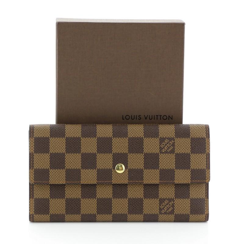 This Louis Vuitton Porte Tresor International Wallet Damier, crafted from damier ebene coated canvas, features a flap top and gold-tone hardware. Its snap closure opens to a brown leather interior with multiple card slots, long flat pockets, and pen
