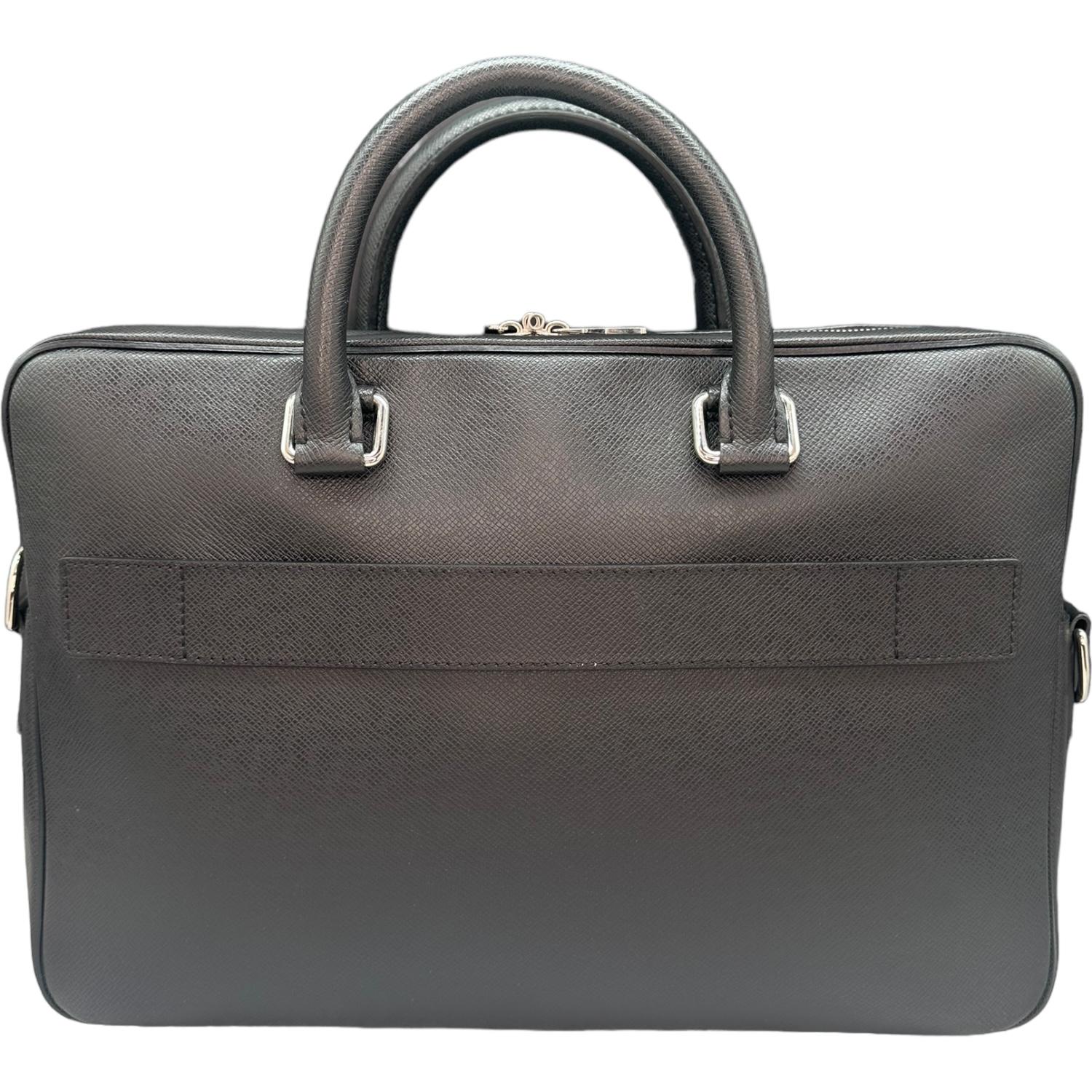 This Louis Vuitton Porto Document Business bag is finely crafted of black Louis Vuitton Taiga leather exterior with leather trimming and Gun metal-tone hardware. It has dual rolled leather top handles. It features a zip pocket on the front and a