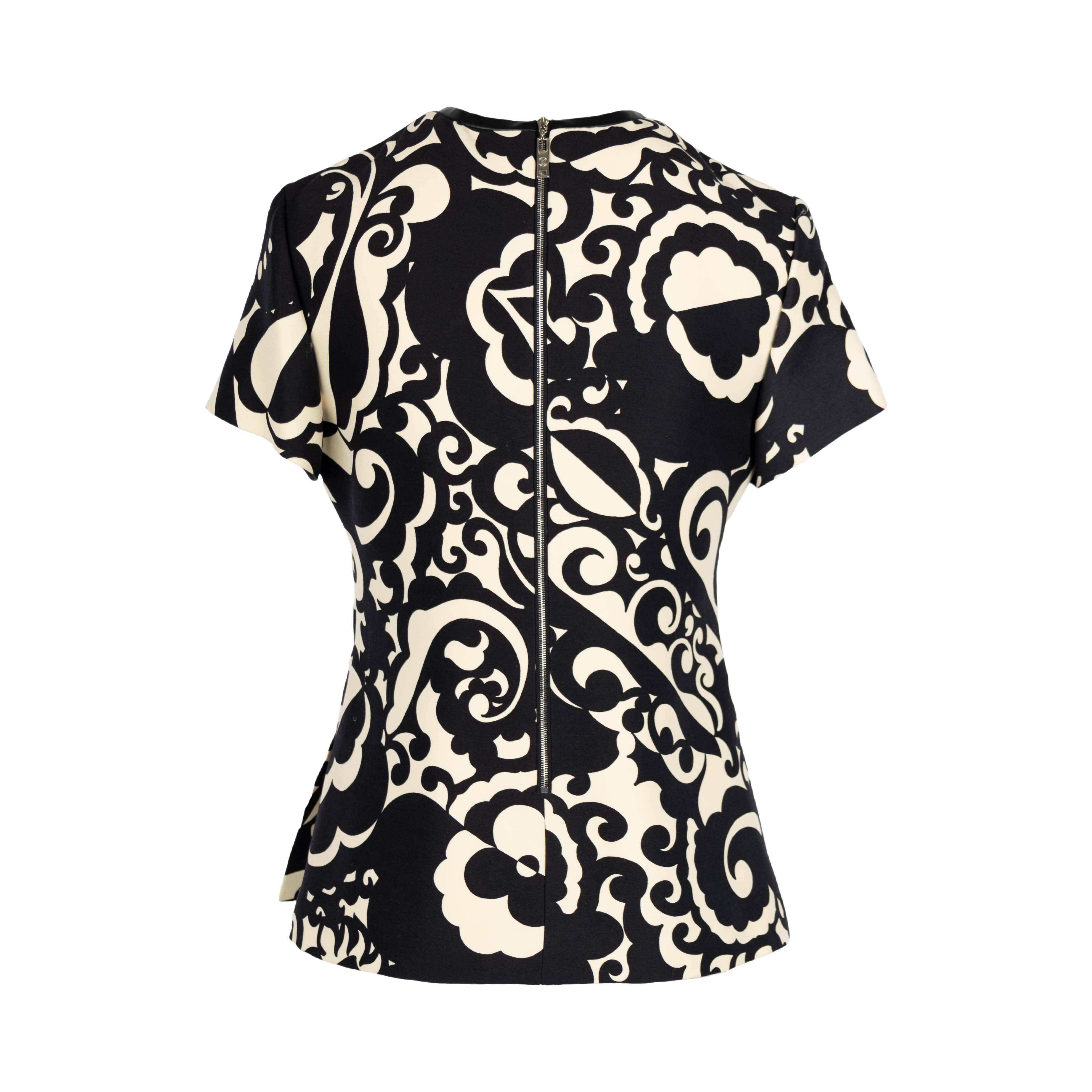 This blouse showcases a contemporary t-shirt silhouette, detailed with an optical flower print and the brand's iconic flower inlay. Its neckline is accented with leather, and side slits add a bold feminine touch.Remarks: New with Tag
 
