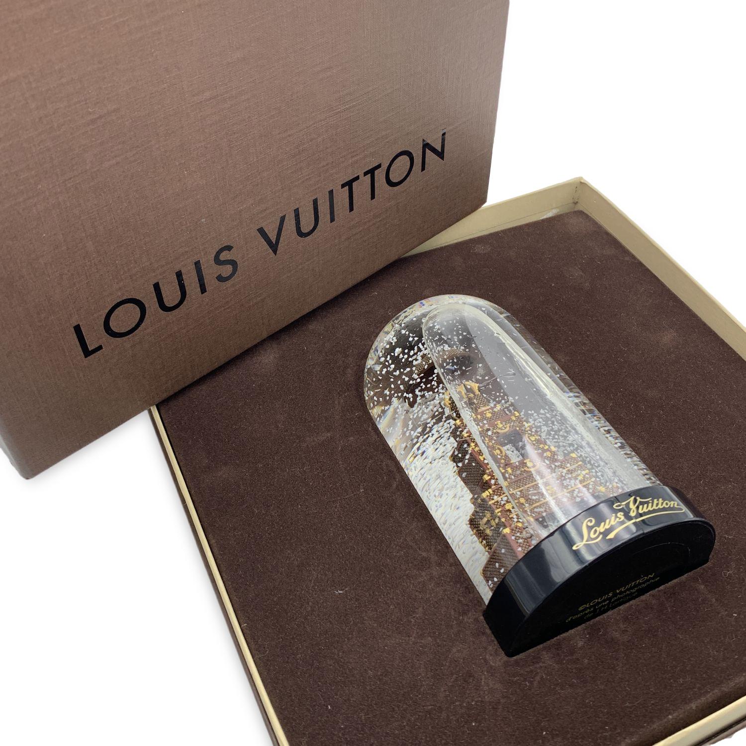 Louis Vuitton snow globe with a miniature reproduction of the iconic Louis Vuitton suitcase and trunks. . It is made of clear glass with a black plastic base. 'Louis Vuitton' signature on the base. Made to celebrate the 1st anniversary of the