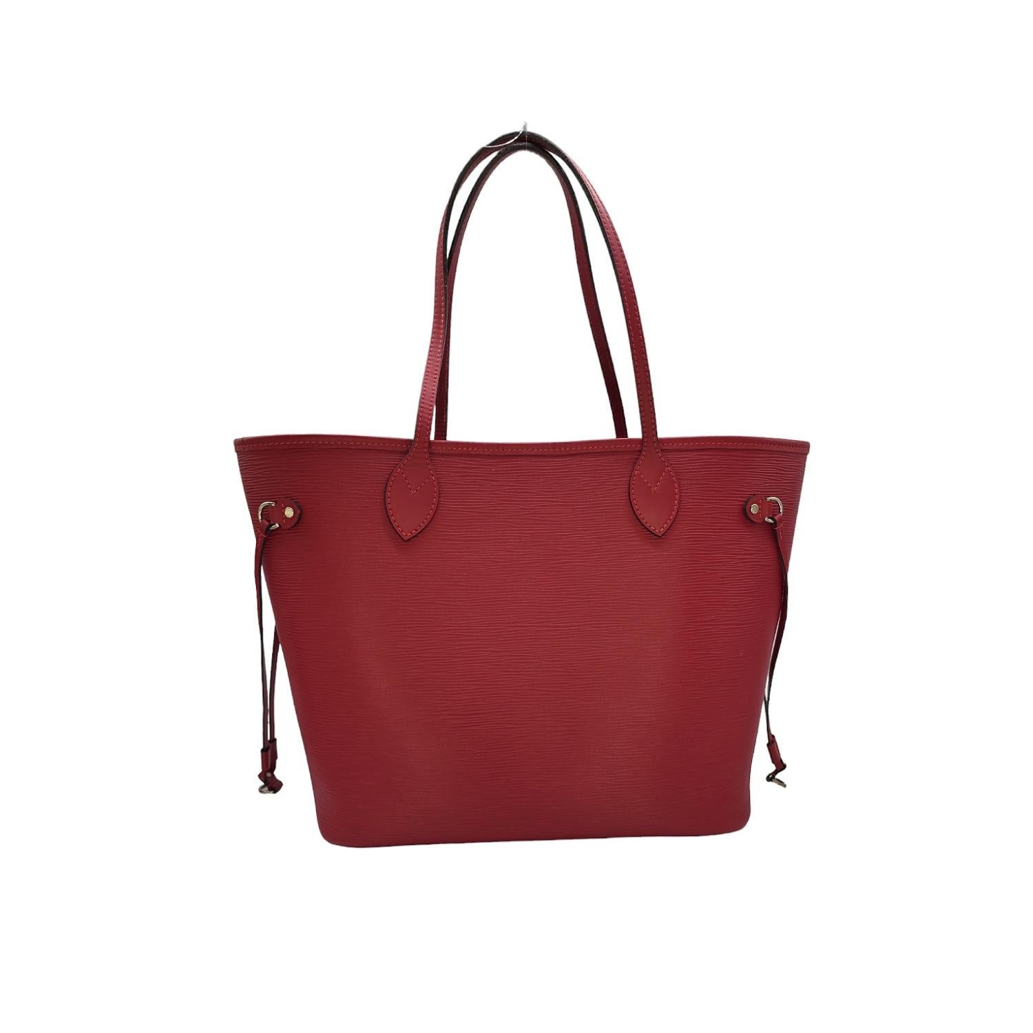 Questa elegante tote è realizzata in pelle con texture Epi di colore rosso, nella misura media. La tote è caratterizzata da manici in pelle di vacchetta liscia, finiture e cordoncini laterali con finiture in argento lucido. L'ampia parte superiore