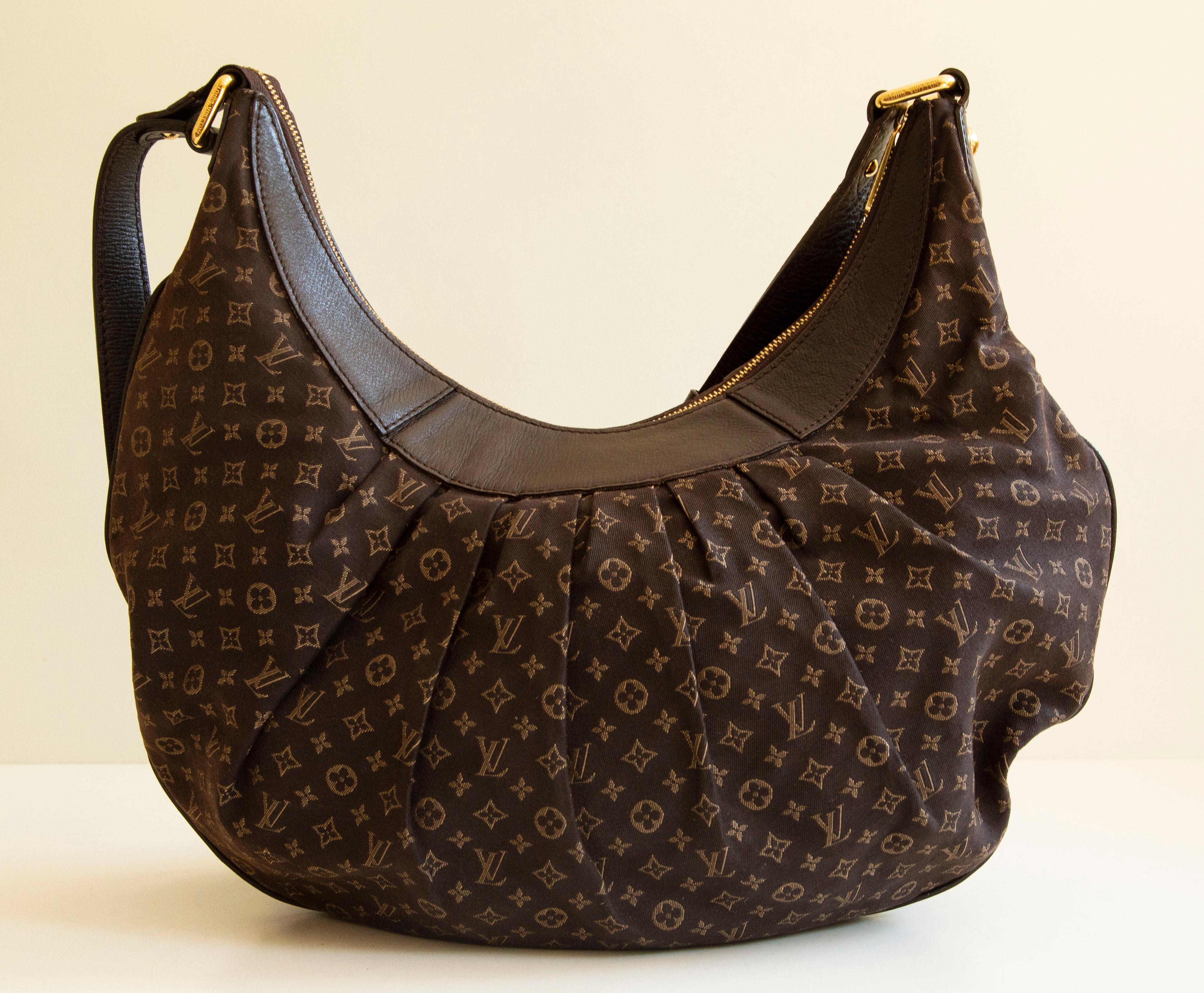 An authentic Louis Vuitton Rhapsody MM. The bag features an Idylle Monogram canvas, brown leather trim, and gold-toned hardware. The interior is lined with brown fabric and there are two slip pockets inside. The interior is neat & clean. The
