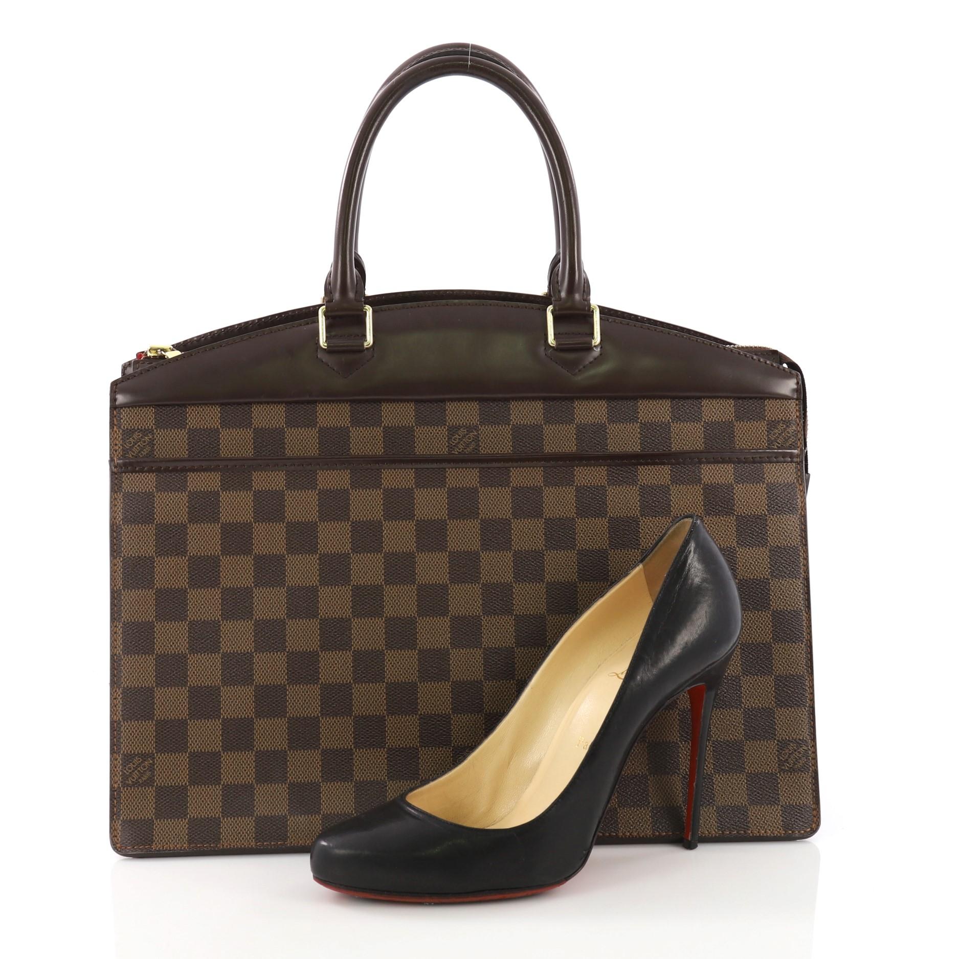 This Louis Vuitton Riviera Handbag Damier, crafted in damier ebene coated canvas, features dual top handles and gold-tone hardware. Its zip closure opens to a red leather interior with slip pockets. **Note: Shoe photographed is used as a sizing