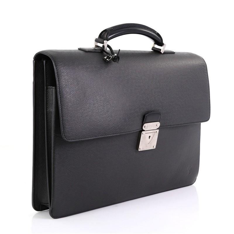 This Louis Vuitton Robusto 1 Briefcase Taiga Leather, crafted in black taiga leather, features leather top handle with links, exterior back flat pocket, and silver-tone hardware. Its S-lock closure opens to a black fabric interior divided into two
